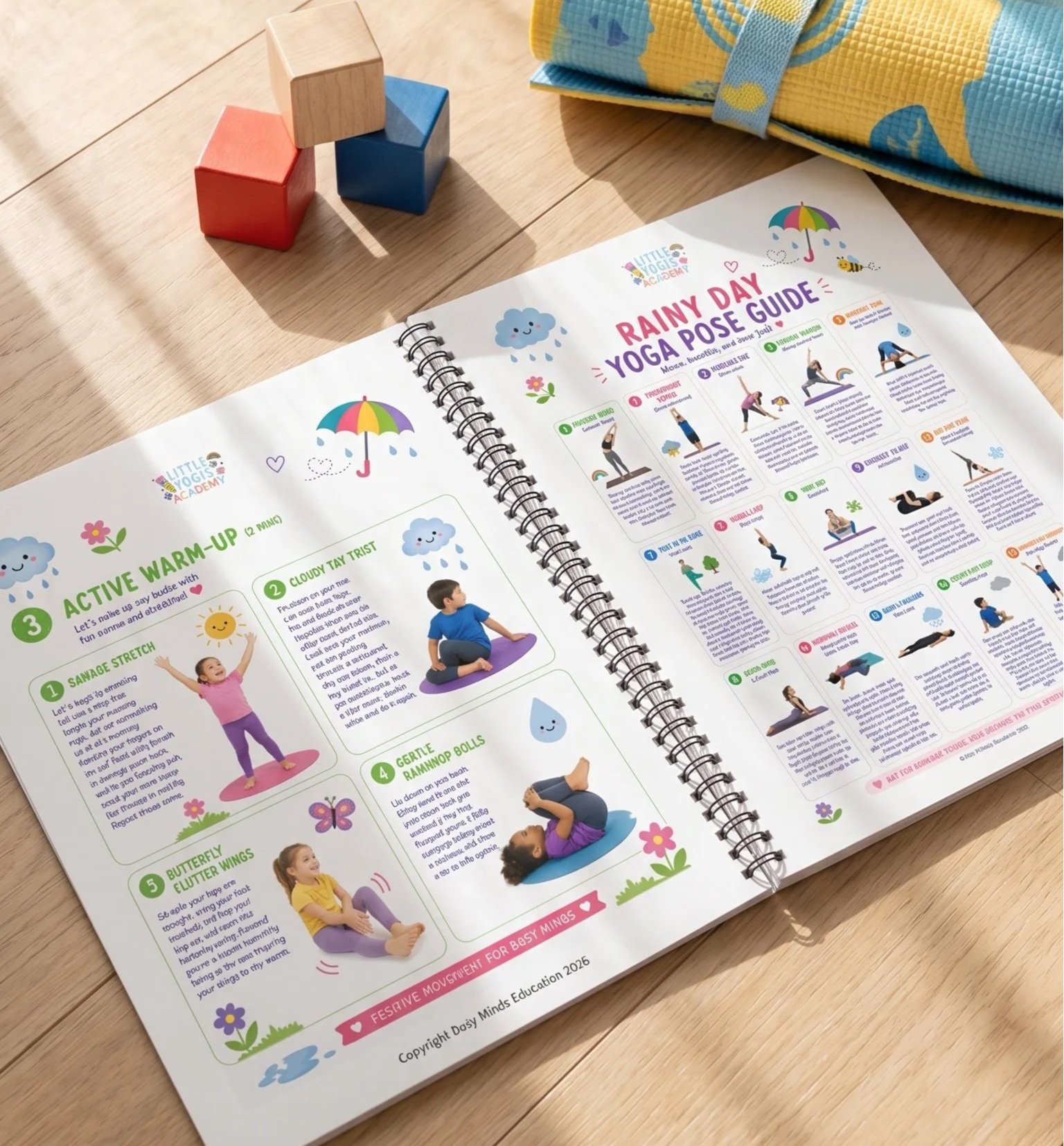 Open spiral-bound booklet titled Rainy Day Yoga Pose Guide with colorful illustrations of children performing various yoga poses on a wooden surface. The booklet is surrounded by small colorful toys and a folded fabric item.