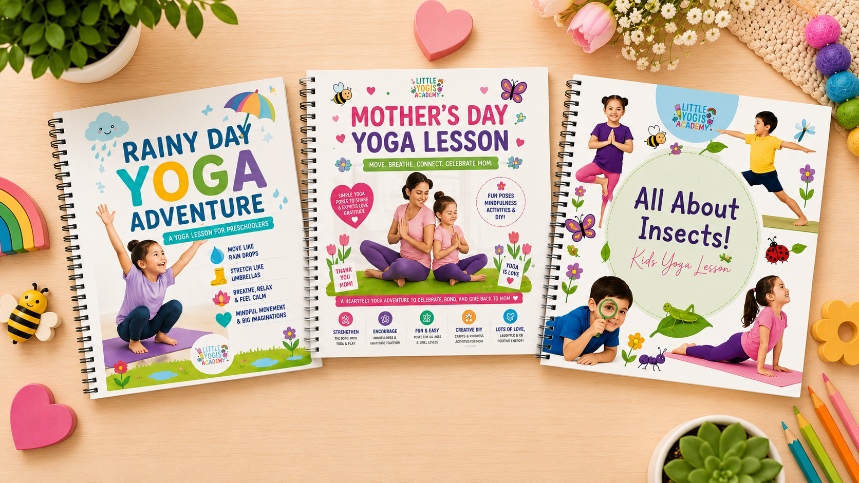 Three spiral notebooks with colorful covers on a wooden surface, surrounded by various small decorative items like felt hearts, a rainbow, bees, ladybugs, flowers, and colored pencils. The notebooks feature children practicing yoga on brightly colored backgrounds, with titles related to rain, Mother's Day, and insects.