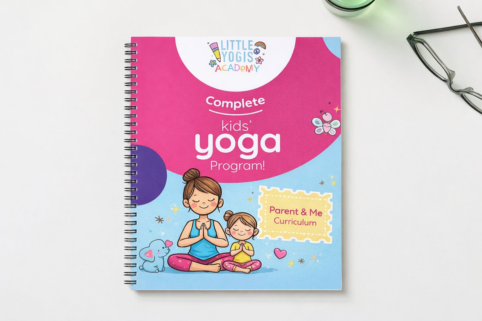 A children's yoga program book titled 'Little Yogis Academy.' The cover features an illustration of a woman and a girl sitting in a yoga pose with hands together, surrounded by colorful hearts, stars, a butterfly, and a dog. The background is a mix of pink and light blue colors, and the book includes a 'Parent & Me Curriculum' subtitle.