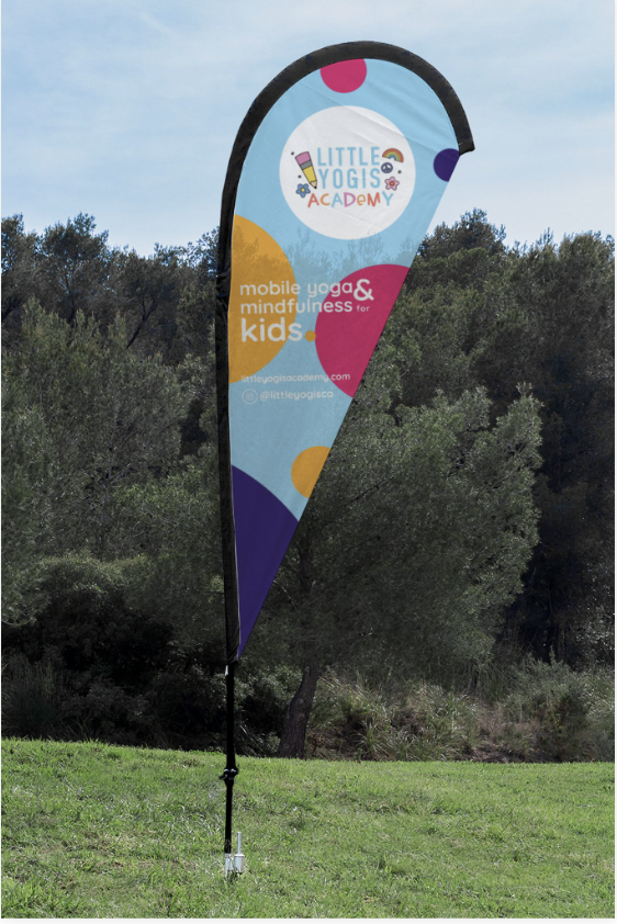 Flag for Little Yoga Academy promoting mobile yoga and mindfulness for kids, set outdoors on grass with trees in the background.