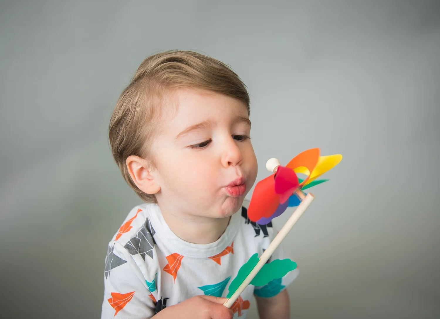 A young boy blowing on a colorful paper pinwheel