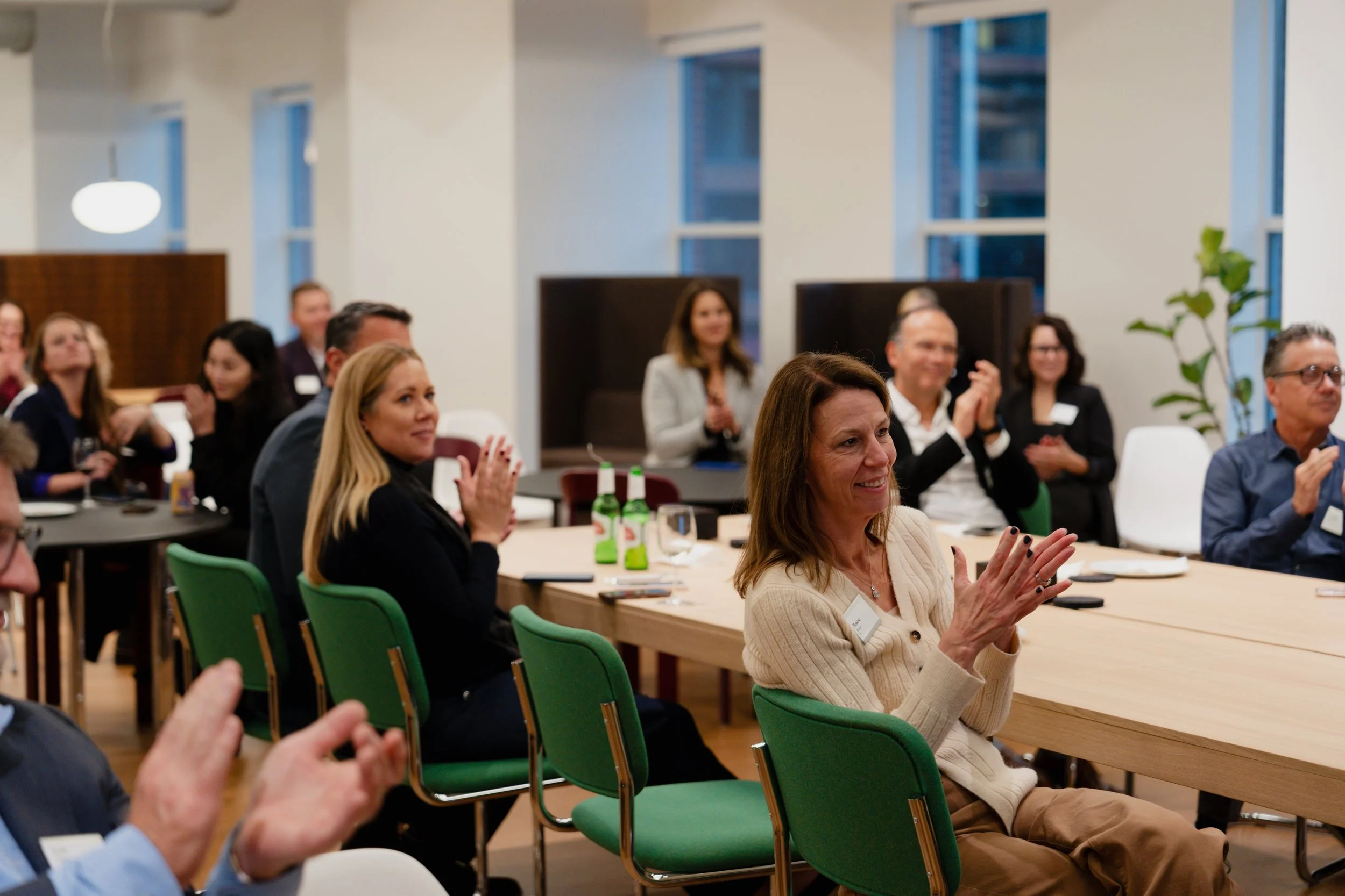 People attending a business or networking event, seated at a large table, clapping and smiling.