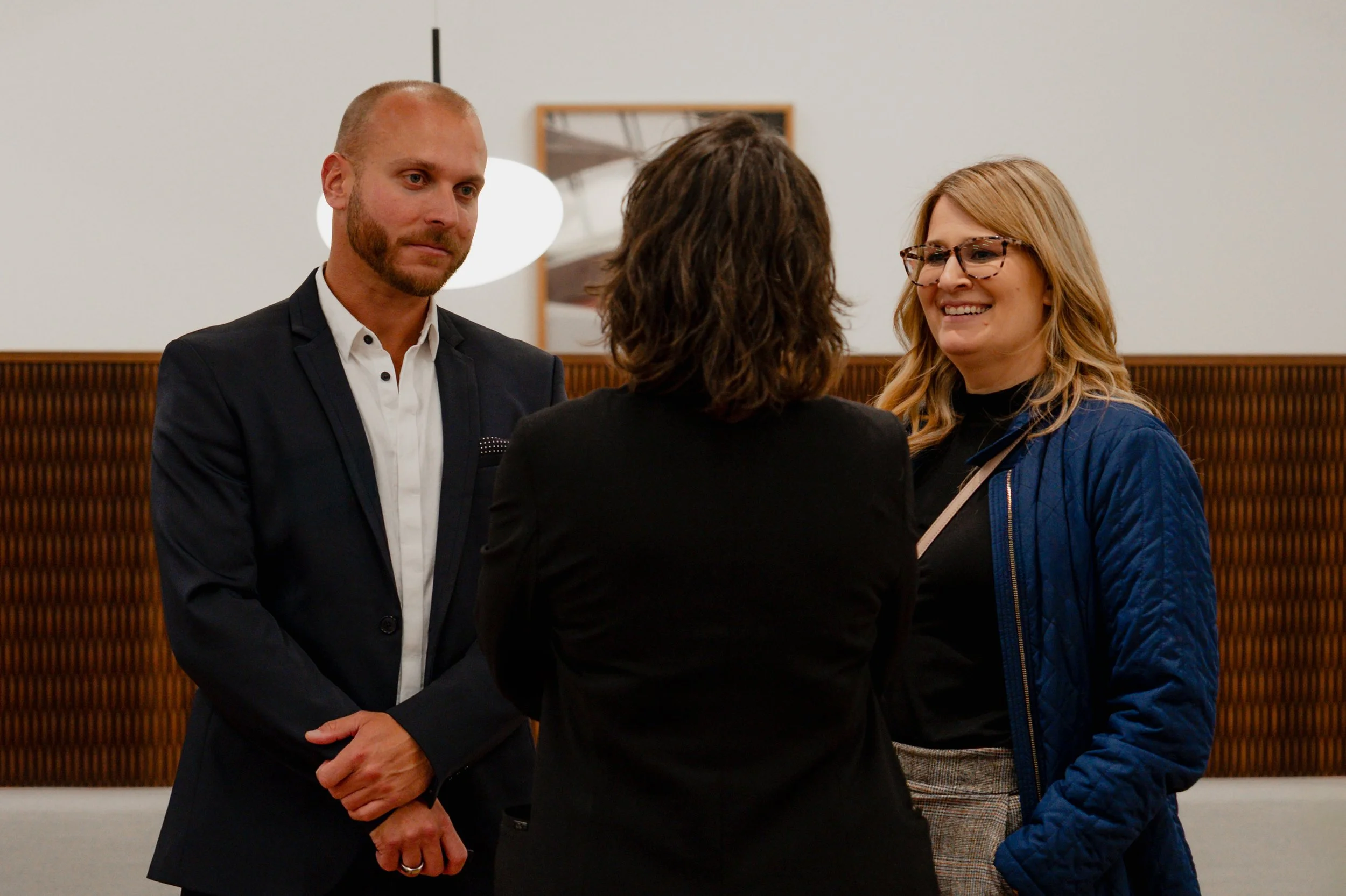 Three people having a conversation at a formal or professional setting, with a woman smiling and two men listening.