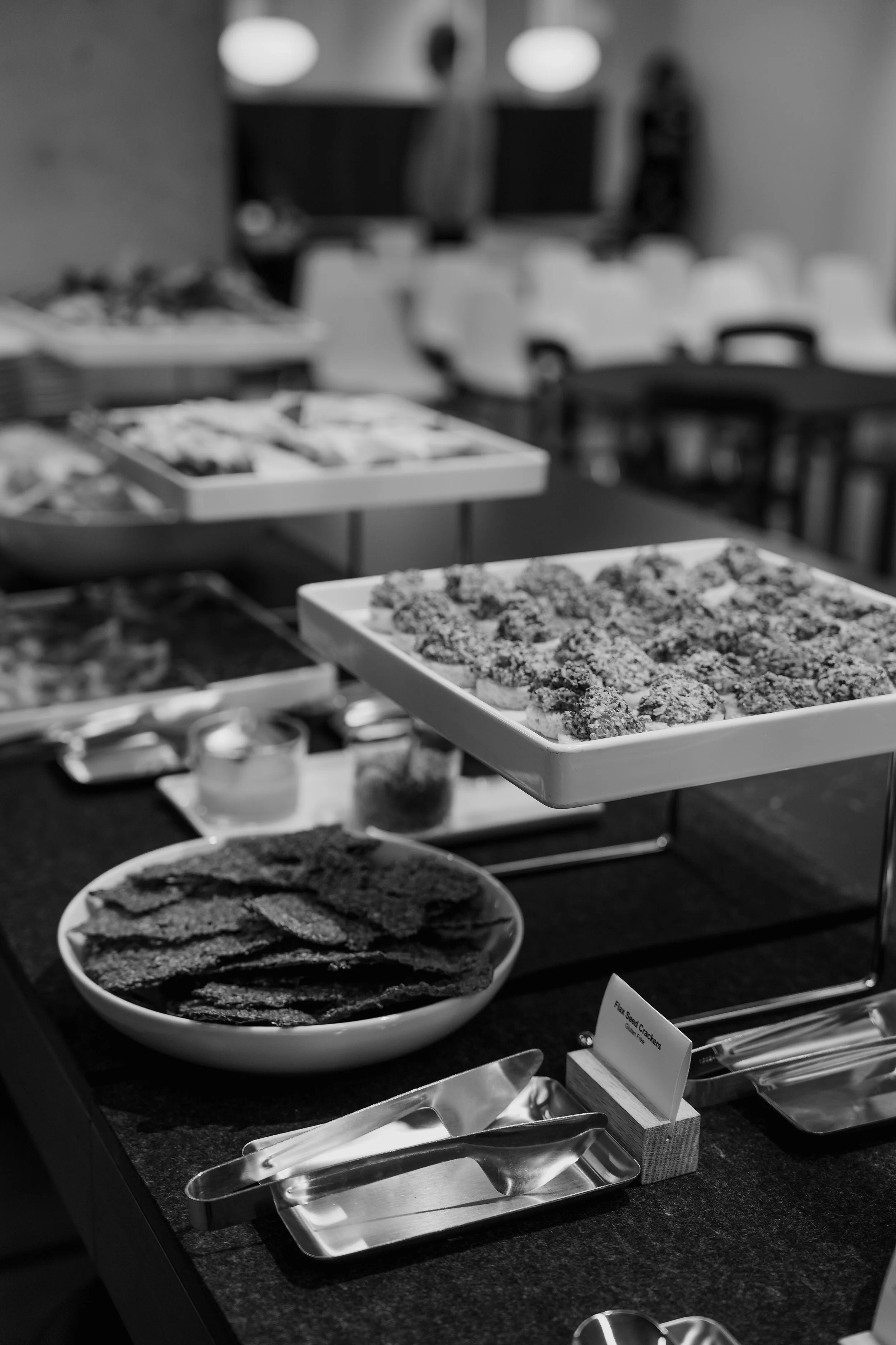 Tray of cookies and bowl of crackers on a table in a buffet setup, with chairs and tables in the background in a conference room or event space.