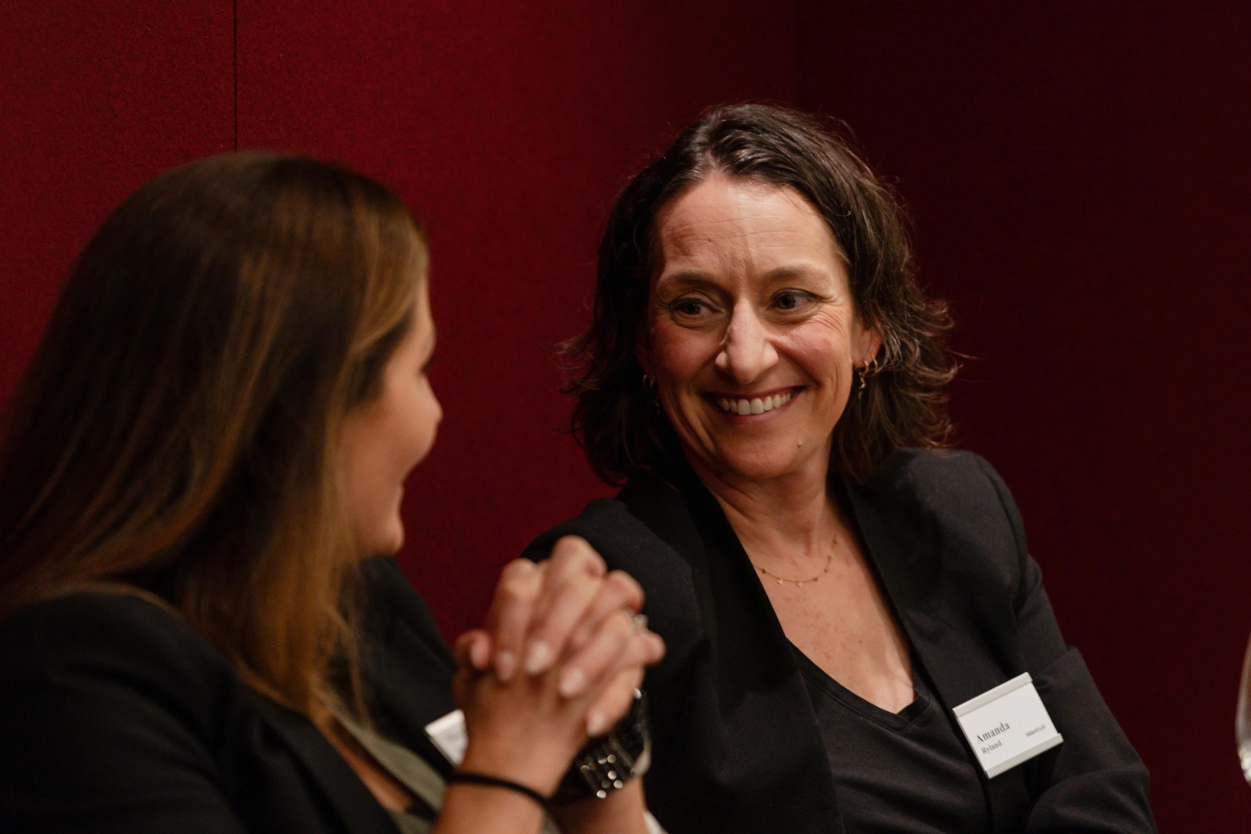 Two women engaged in conversation, one woman smiling warmly at the other in a professional setting.