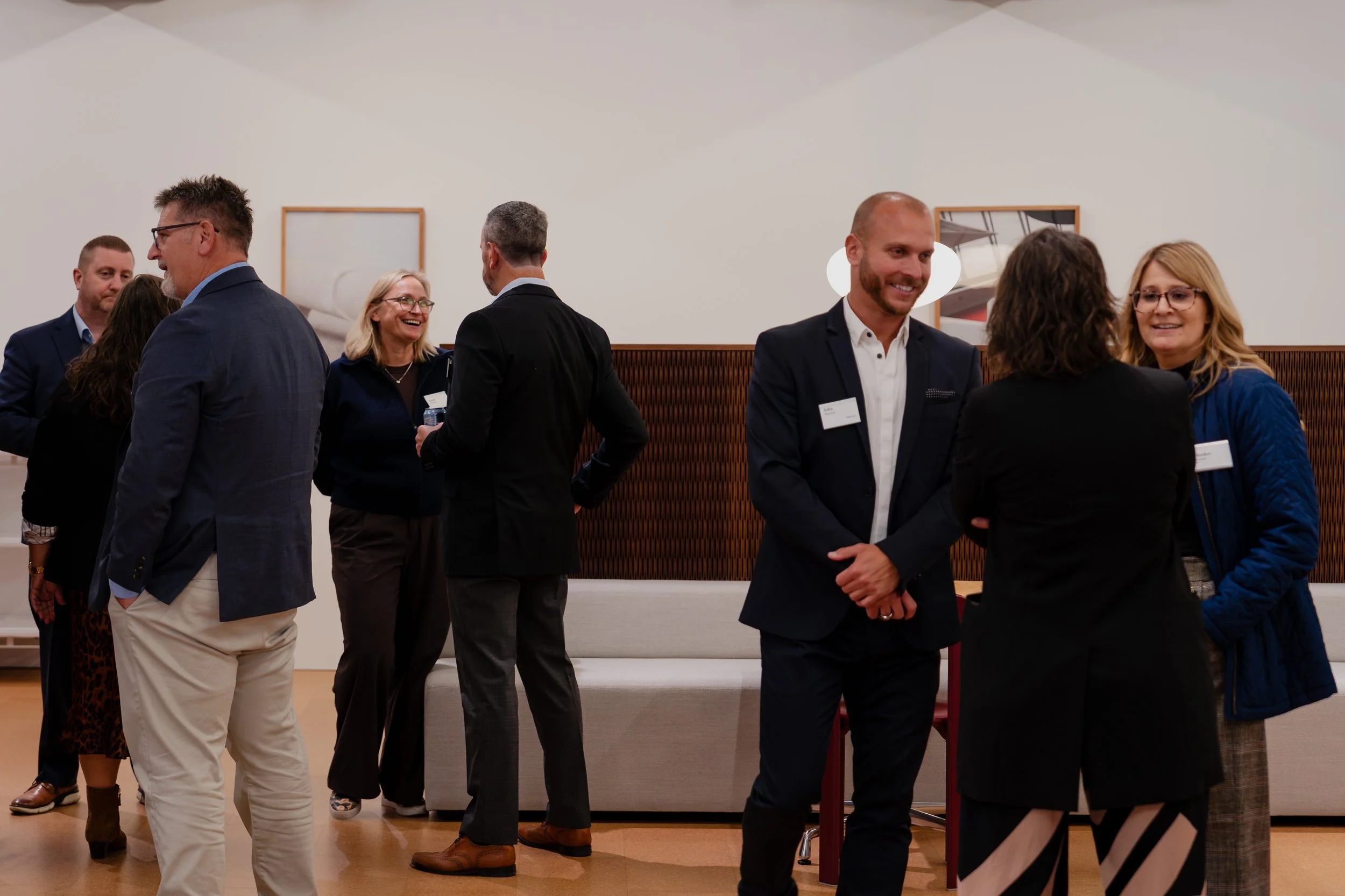 Group of people in business attire socializing and talking at an indoor networking event or conference.