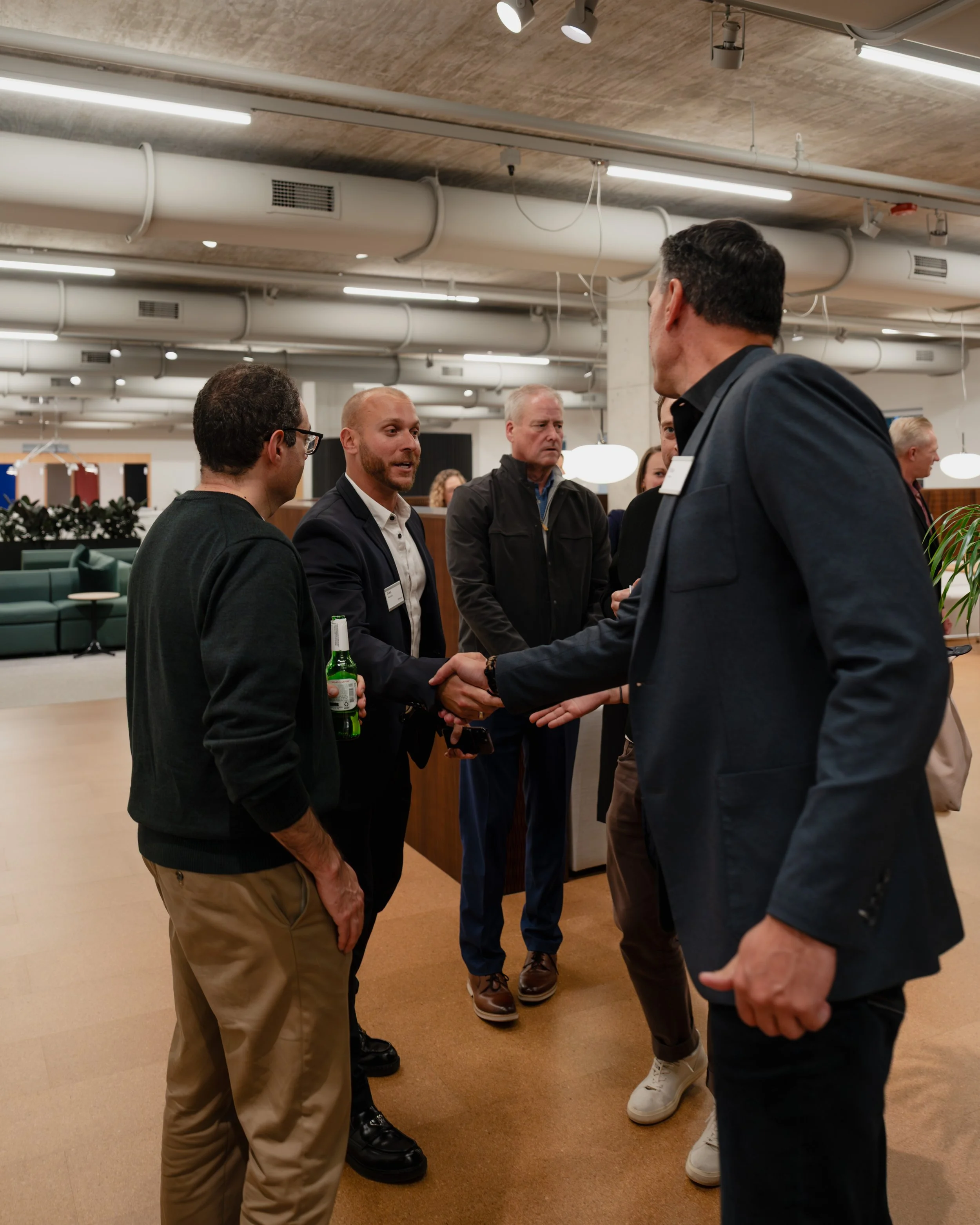 A business networking event with several men shaking hands and engaging in conversation in a modern office or conference space.