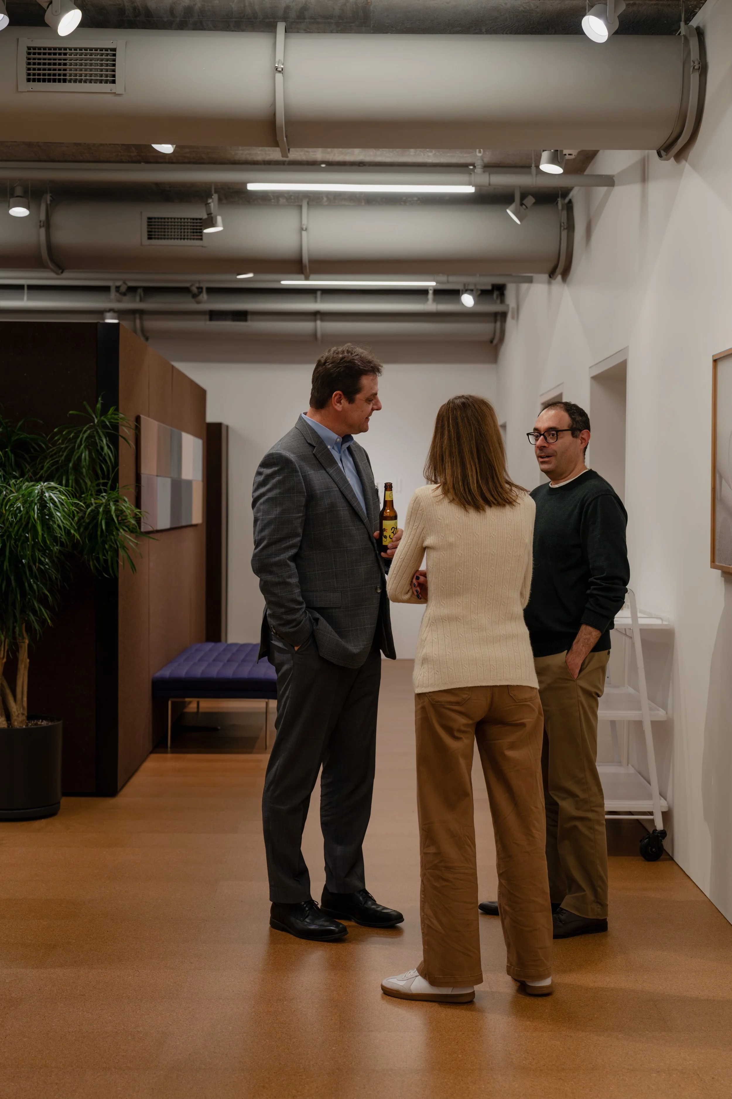 Three people having a conversation in an office with a potted plant and artwork on the wall.