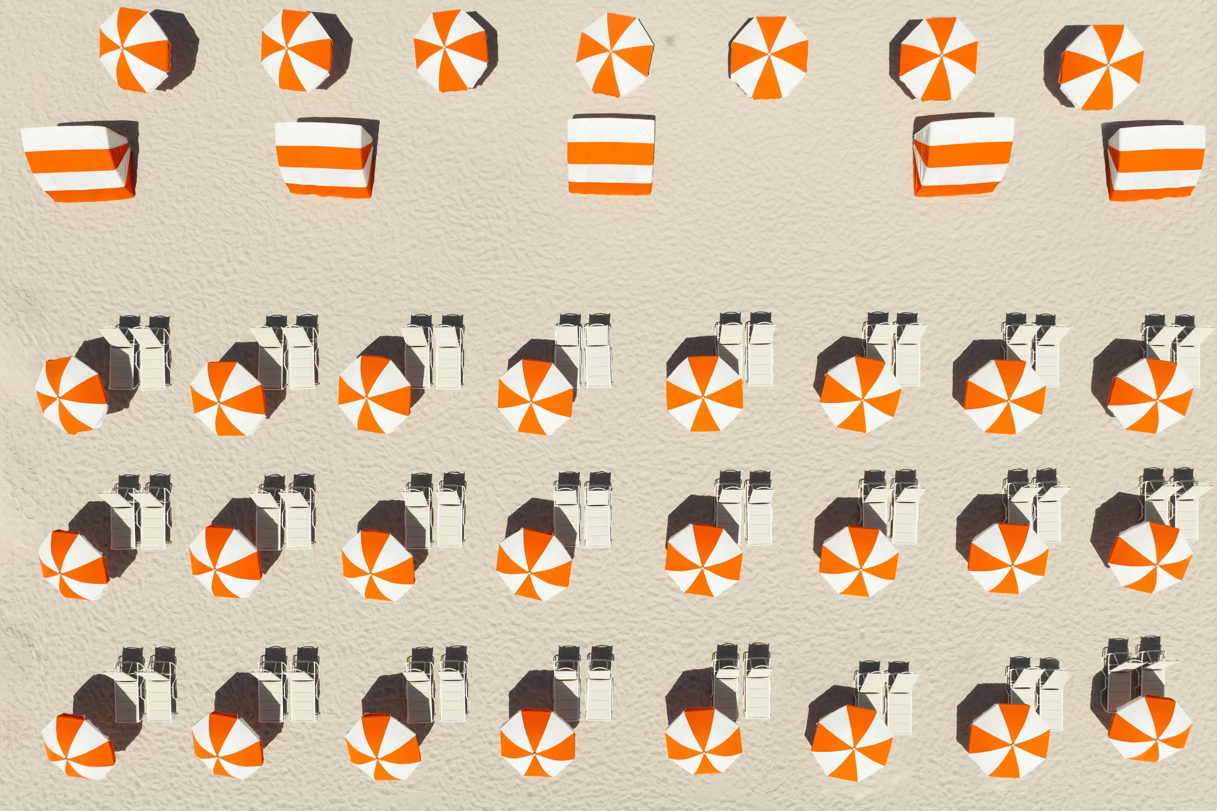 Orange and white beach umbrellas with beach chairs lining the sand at Andaz Miami Beach.