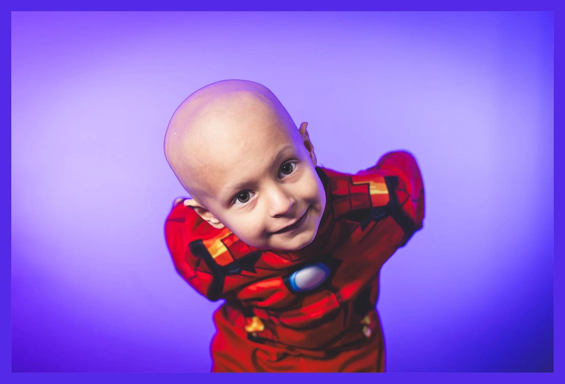 Child in Iron Man costume looking up at camera against purple background.