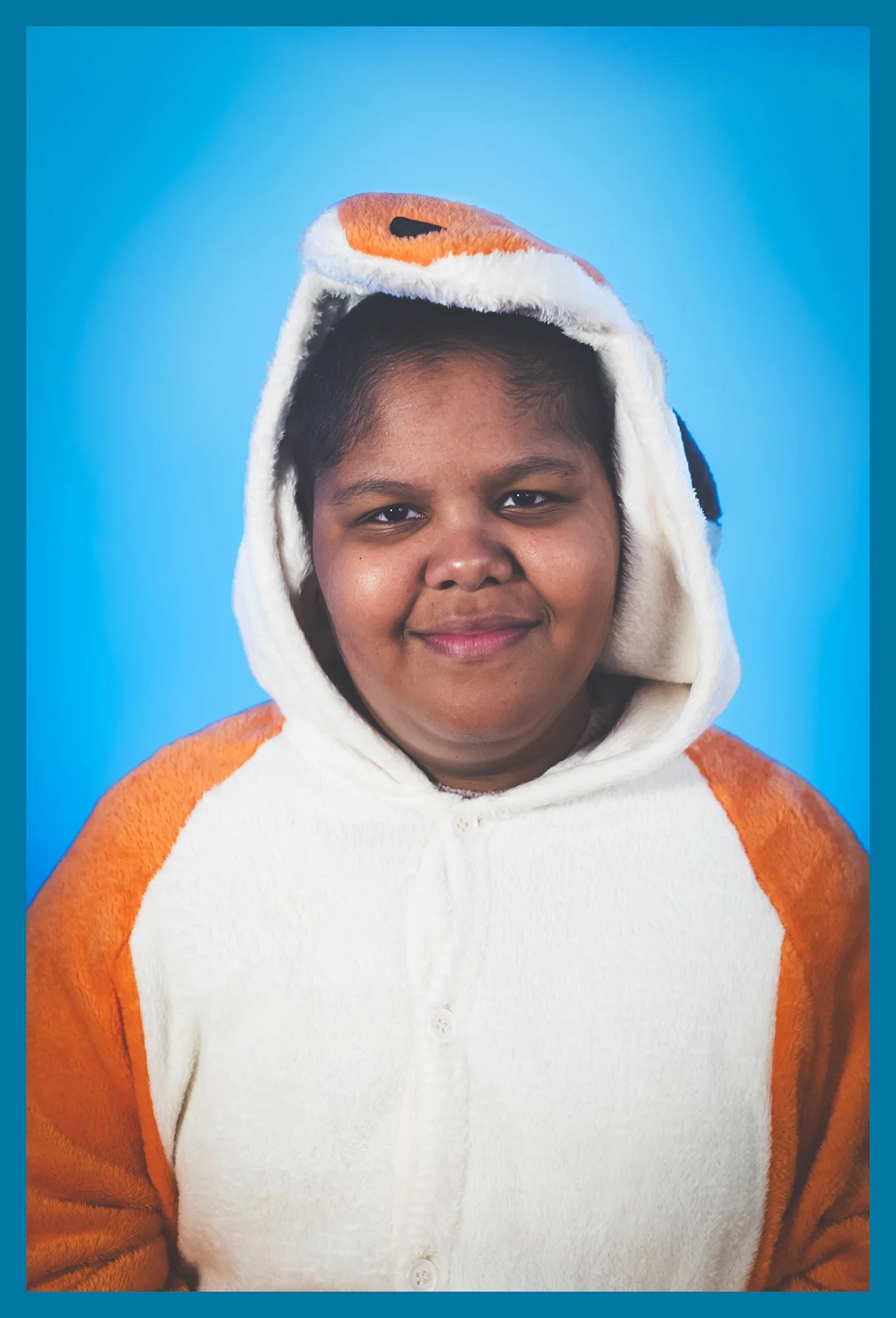 Person wearing a plush animal costume with an orange and white hood, smiling against a blue background.