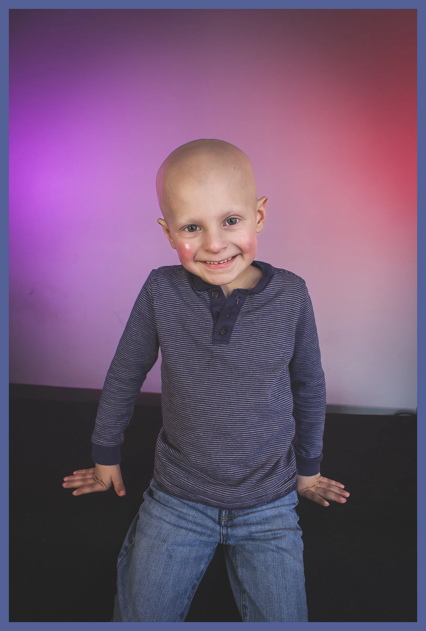 A young boy with a bald head smiling and posing against a colorful, pink and purple gradient background.