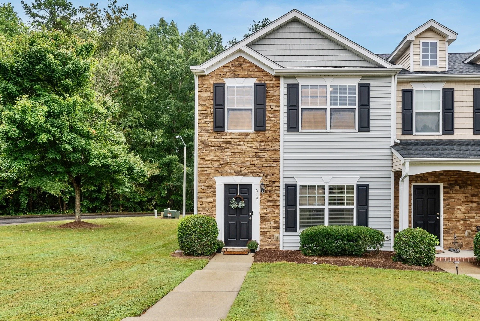 Exterior of a two-story townhouse with a combination of stone and siding facade, black shutters, and well-maintained lawn.