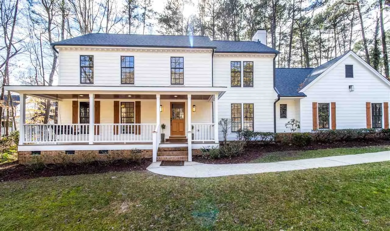 Front view of a two-story white house with a covered porch, surrounded by trees and a well-maintained lawn.