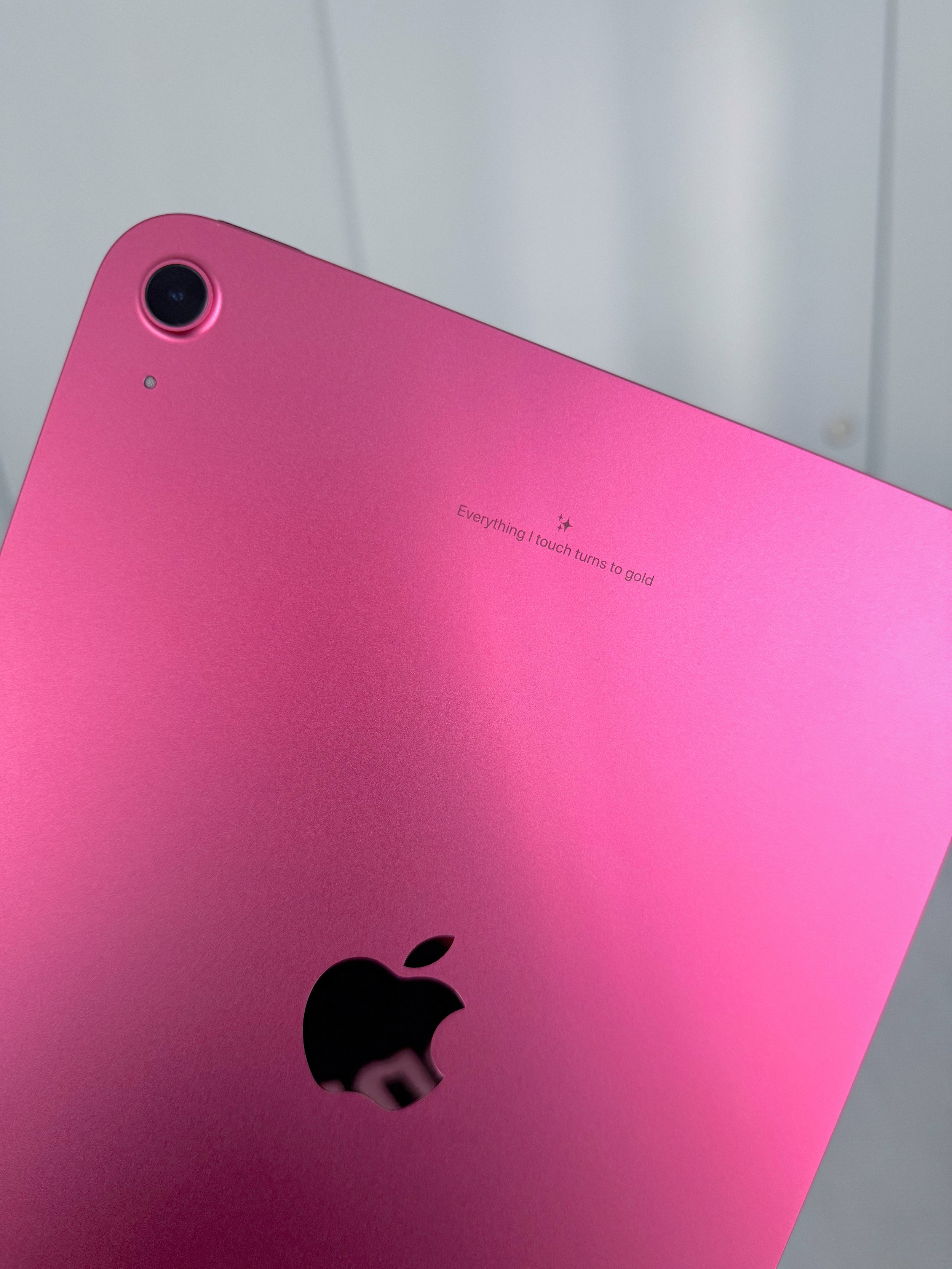Close-up of a pink Apple iPad with a black Apple logo and a rear camera at the top left corner. The back of the iPad has the words 'Everything I touch turns to gold' printed.