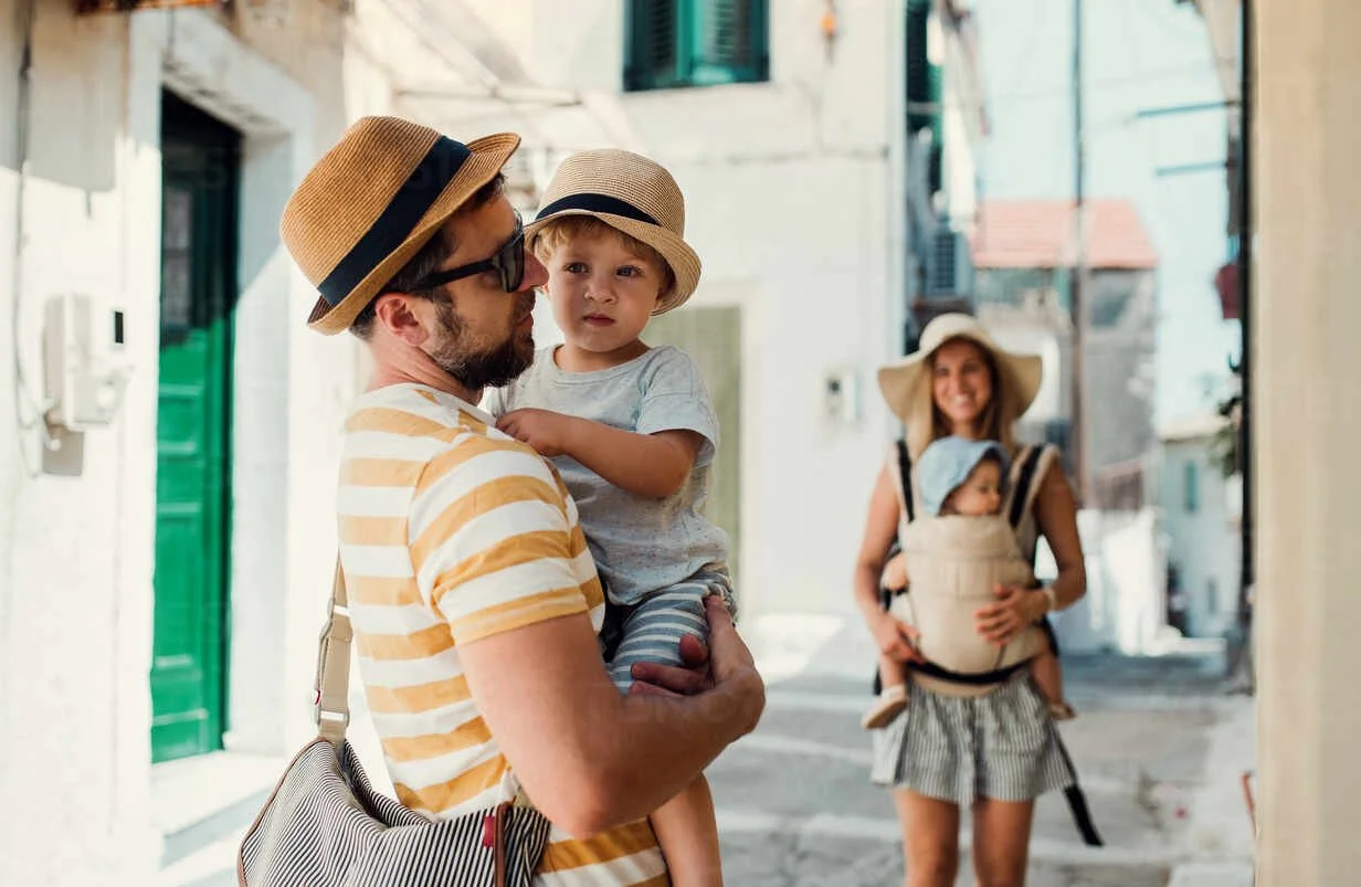 a-family-with-two-toddler-children-walking-in-town-on-summer-holiday-a-father-and-mother-with-son-and-daughter-in-baby-carrier-on-a-narrow-street-HPIF23901.jpg