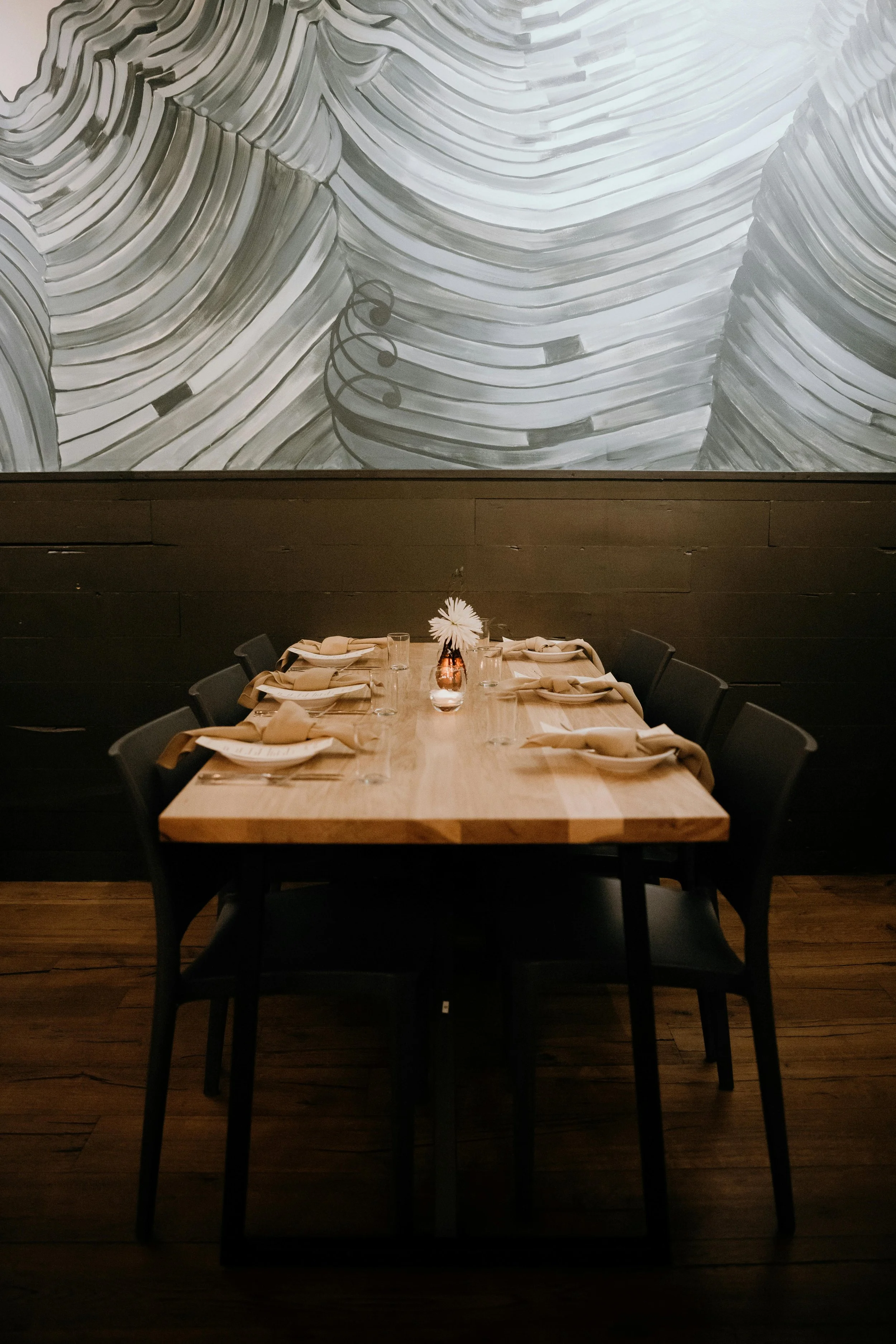 A dining table set for a Midlands based private dining, with beige napkins, glasses, and a small vase with a white flower at the center. Event in Leicester