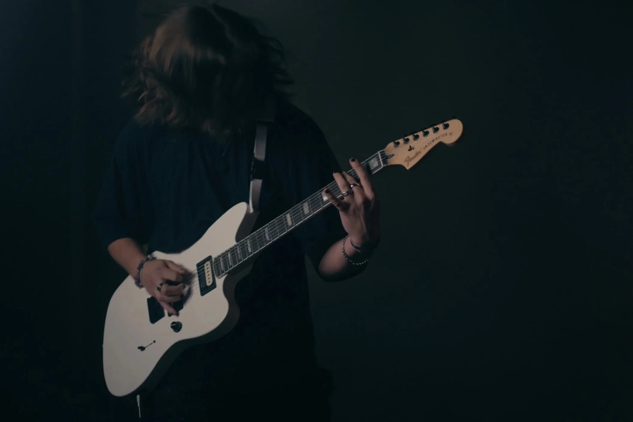 Person spielt Gitarre vor dunklem Hintergrund, Gesicht nicht sichtbar.