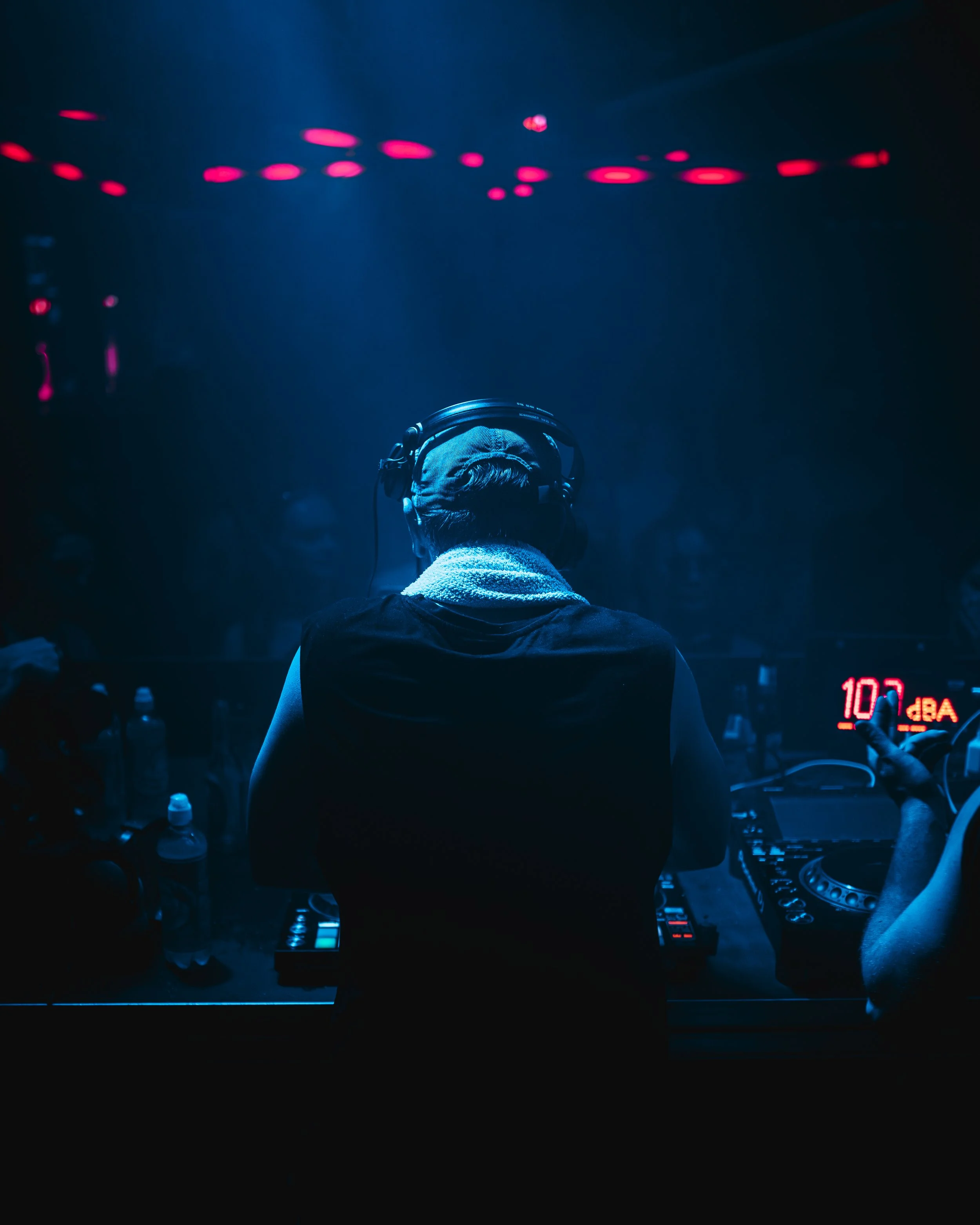 DJ vor einem Mischpult bei einer nächtlichen Party, umgeben von tanzenden Gästen im dunklen Club mit blauen und pinken Lichteffekten.