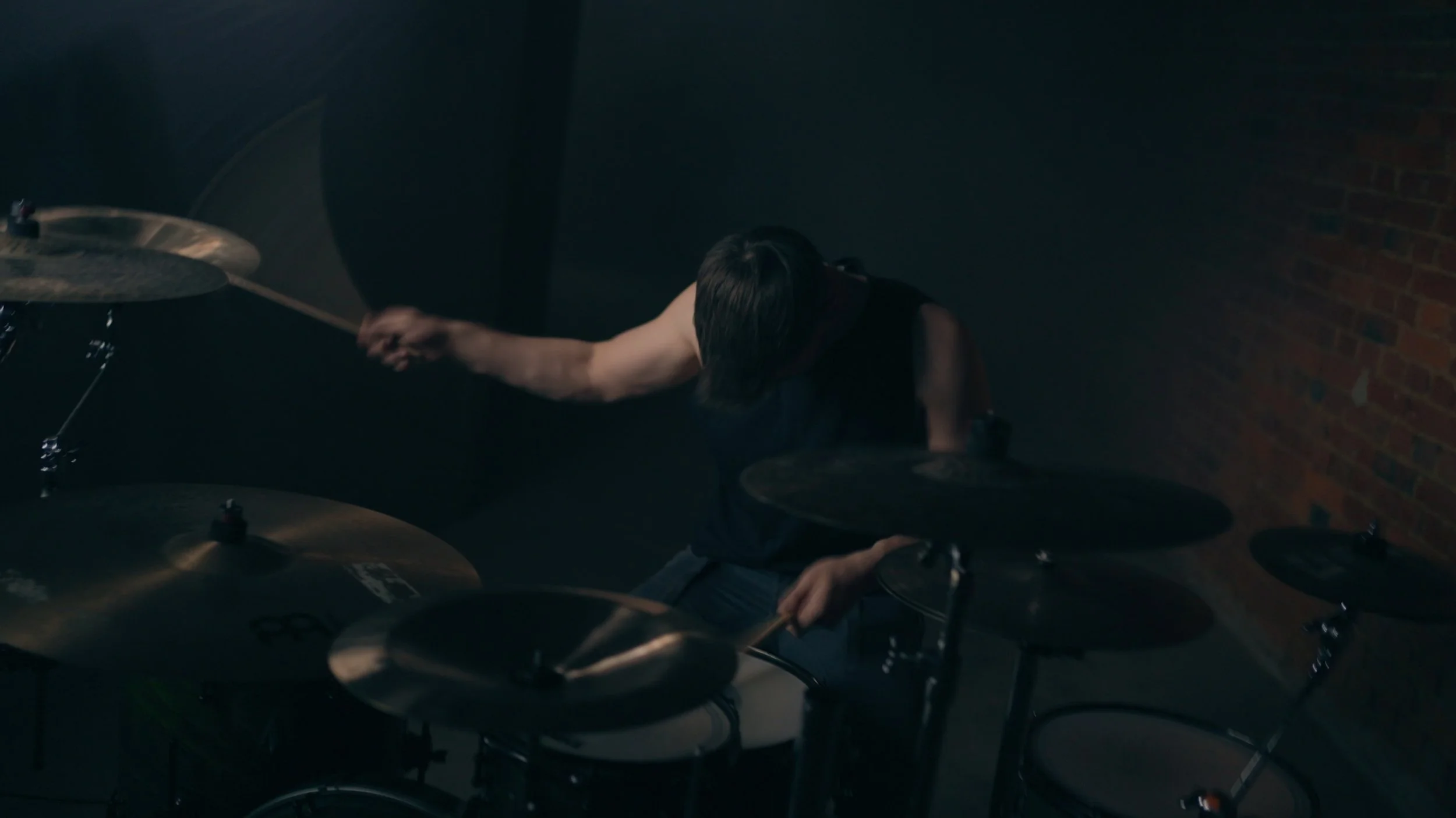 Ein junger Mann spielt Schlagzeug in einem dunklen Raum.