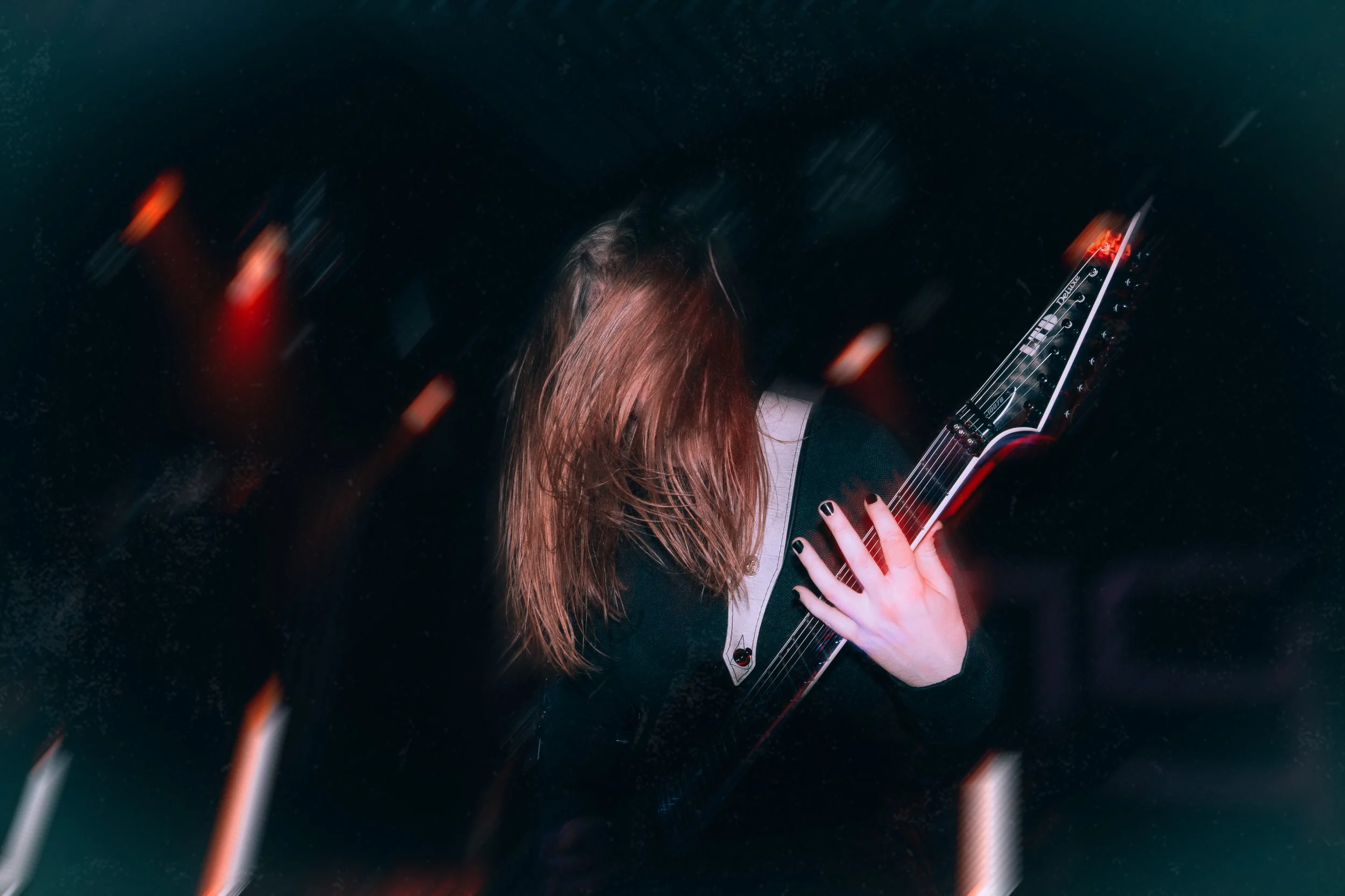 Ein blonder Gitarrist, der Gitarre spielt. Der Hintergrund hat Bewegungsunschärfe, die Farben leuchten. Das Bild ist energiegeladen.