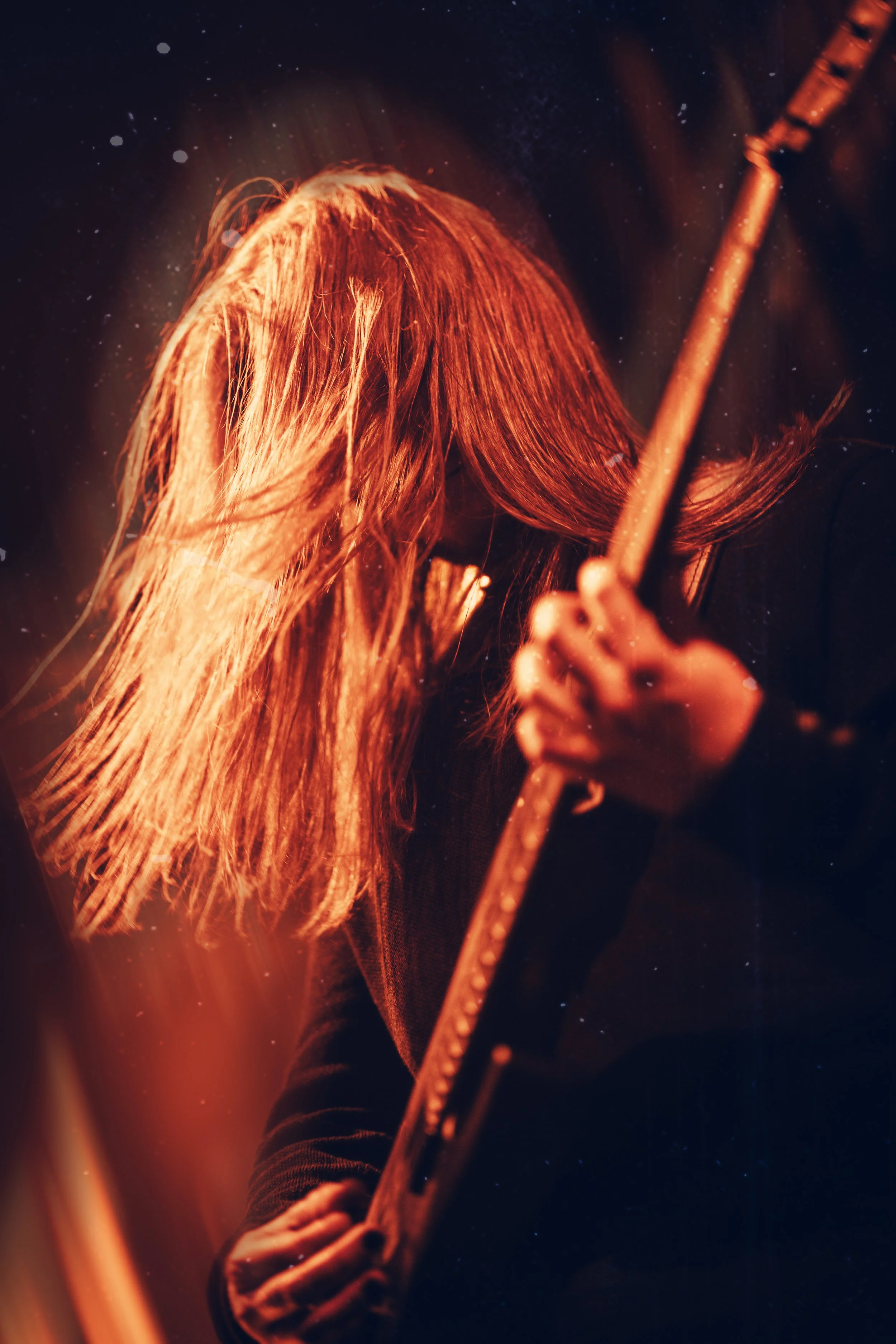 Ein warmes Bild eines Gitarristen auf einem Konzert. Der Gitarrenhals und die Griffhand des Gitarristen sind im Vordergrund. Bewegungen sind schnell.