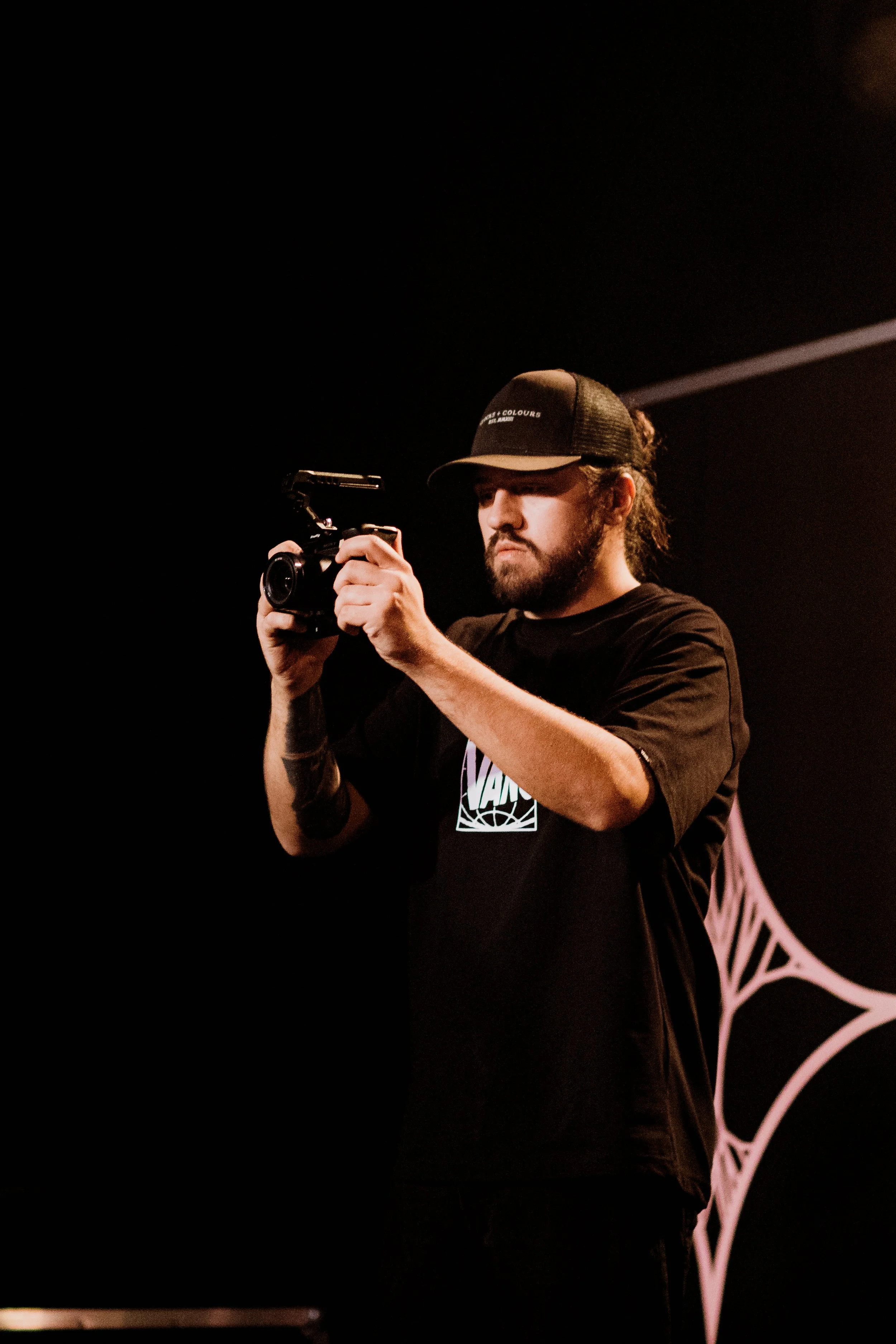 Junger Mann mit Basecap filmt mit Kamera in dunklem Raum.