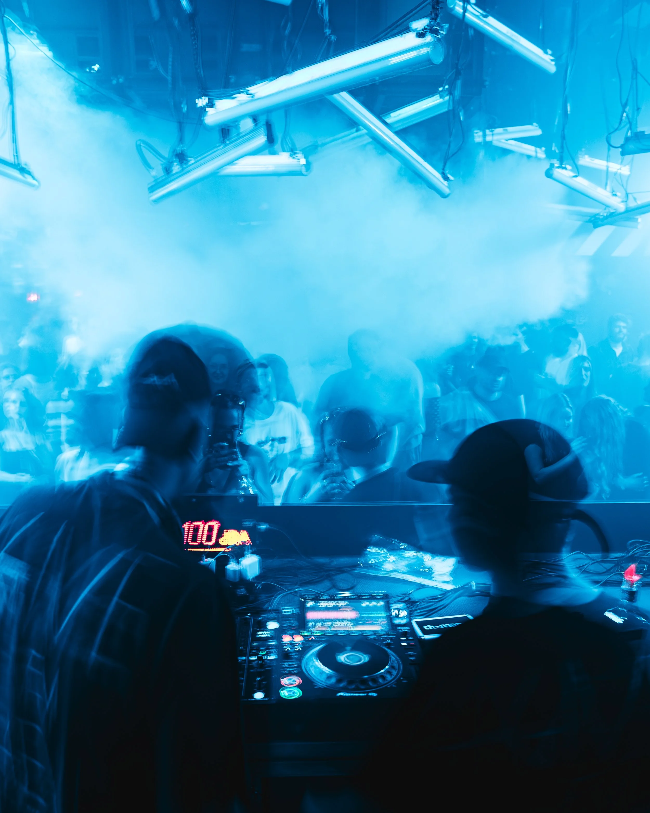 DJ-Setup mit Publikum in einem Club, blaue Beleuchtung, Nebel, dynamische Atmosphäre.