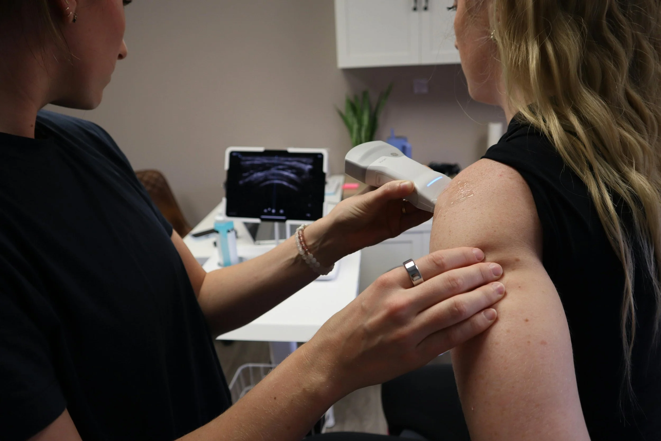 Medical professional conducting an ultrasound on a woman's shoulder in a clinical setting.