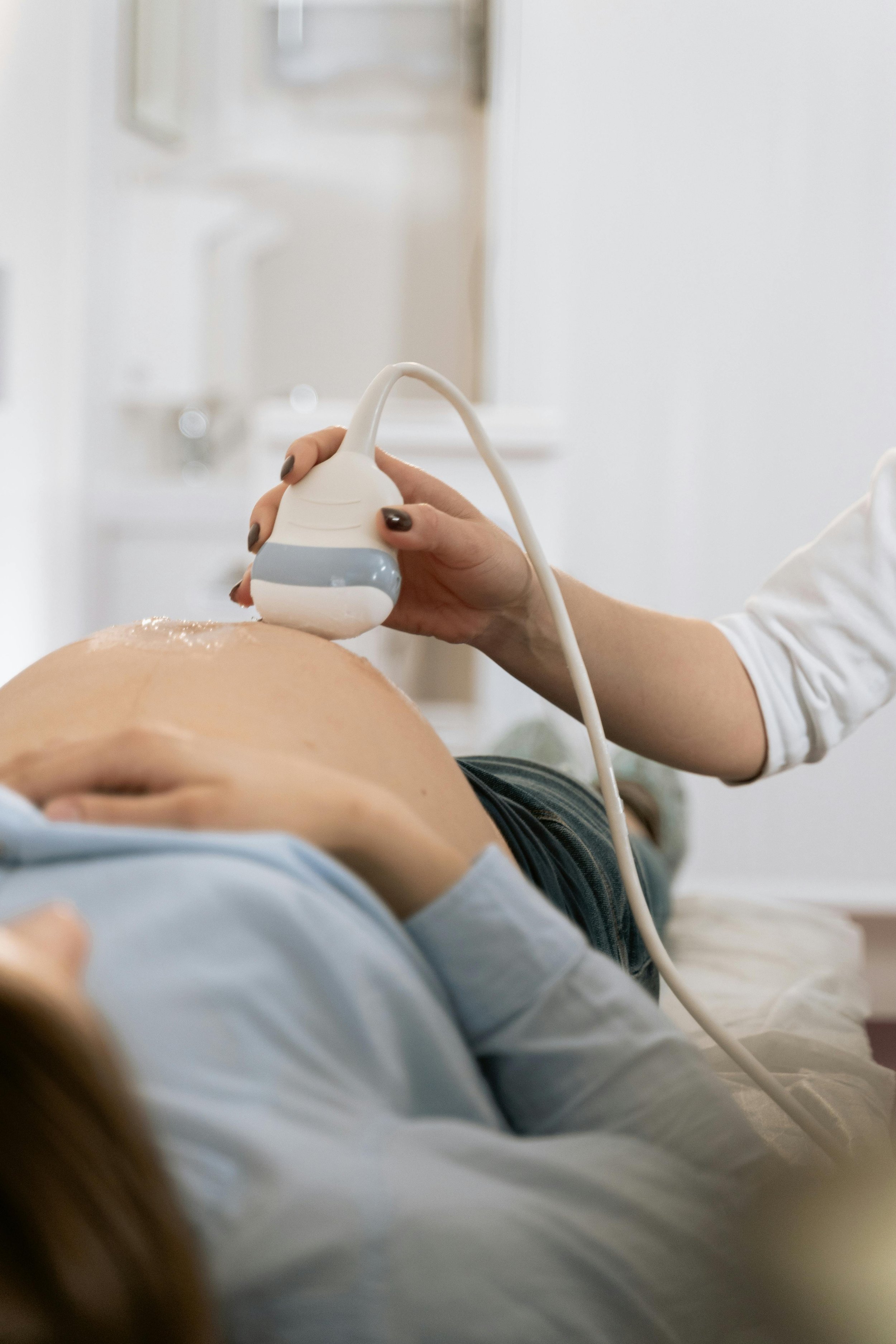 Close up photo of a pregnant woman laying down, with a medical technician conducting an ultrasound exam on her belly. Photo by MART  PRODUCTION: https://www.pexels.com/photo/people-woman-sitting-technology-7089047/