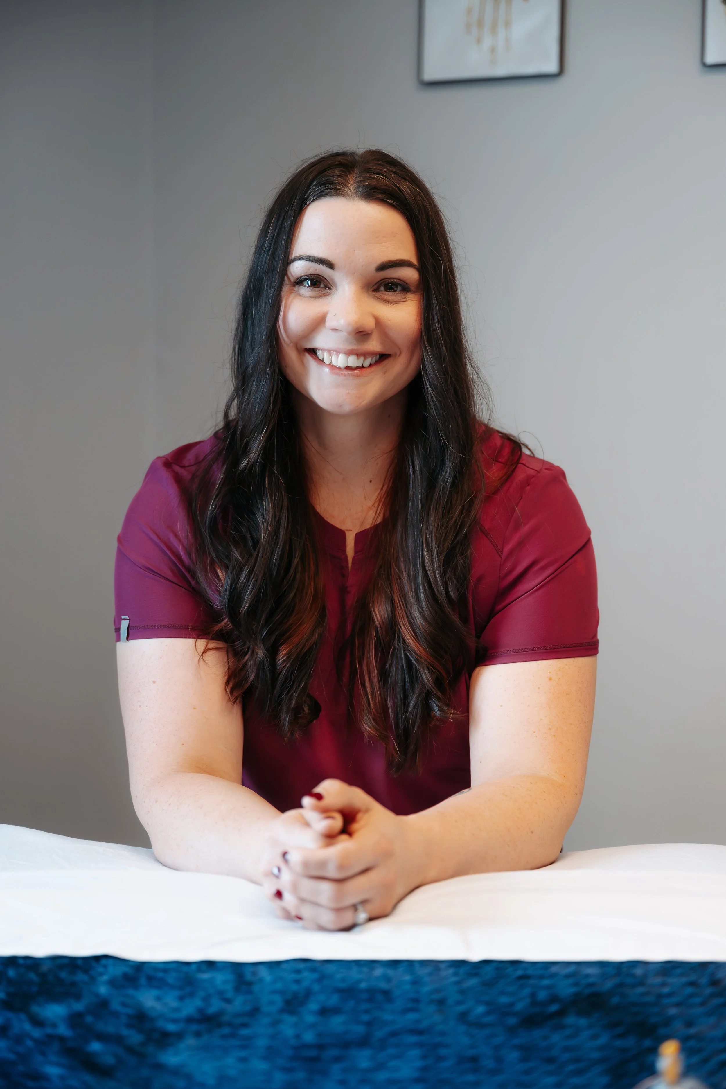 A smiling woman with long dark hair and a maroon shirt sitting at a table.