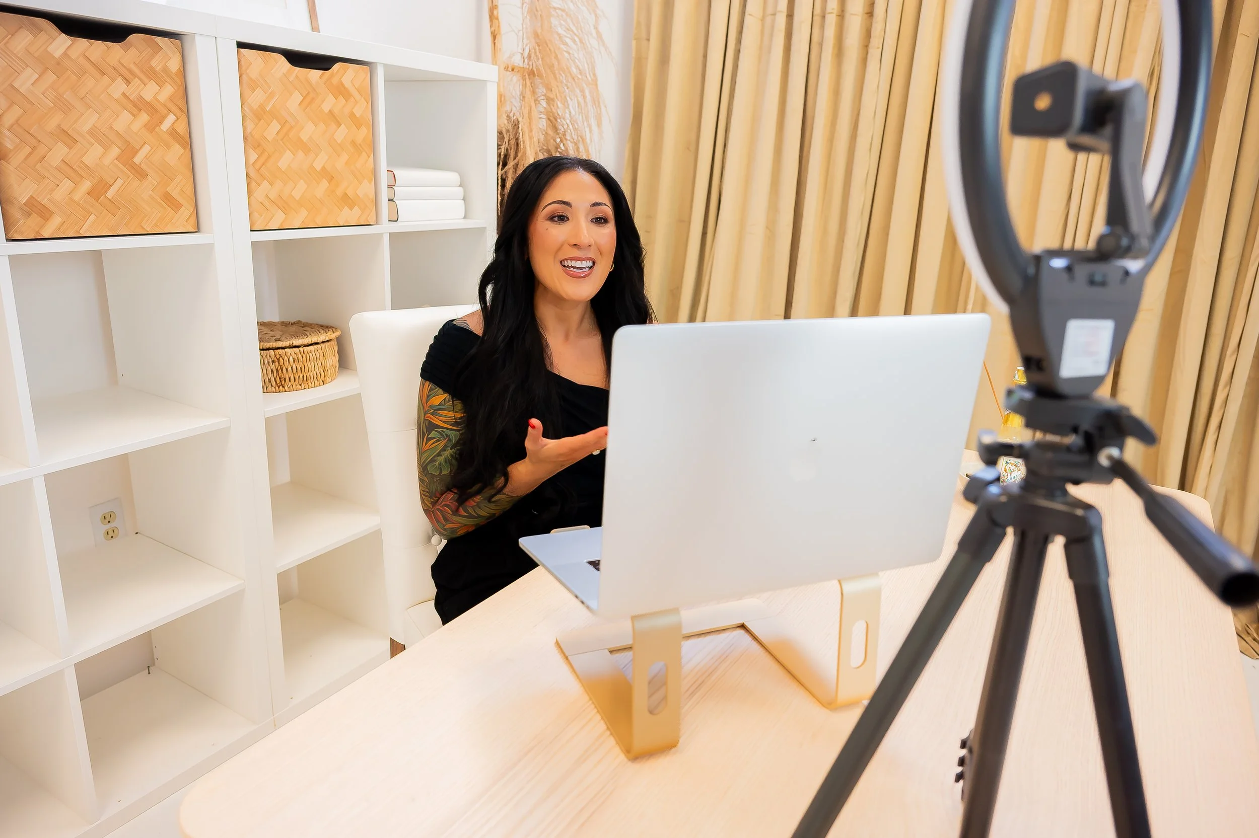 Woman recording a video in front of a camera set up on a tripod with a laptop on a table