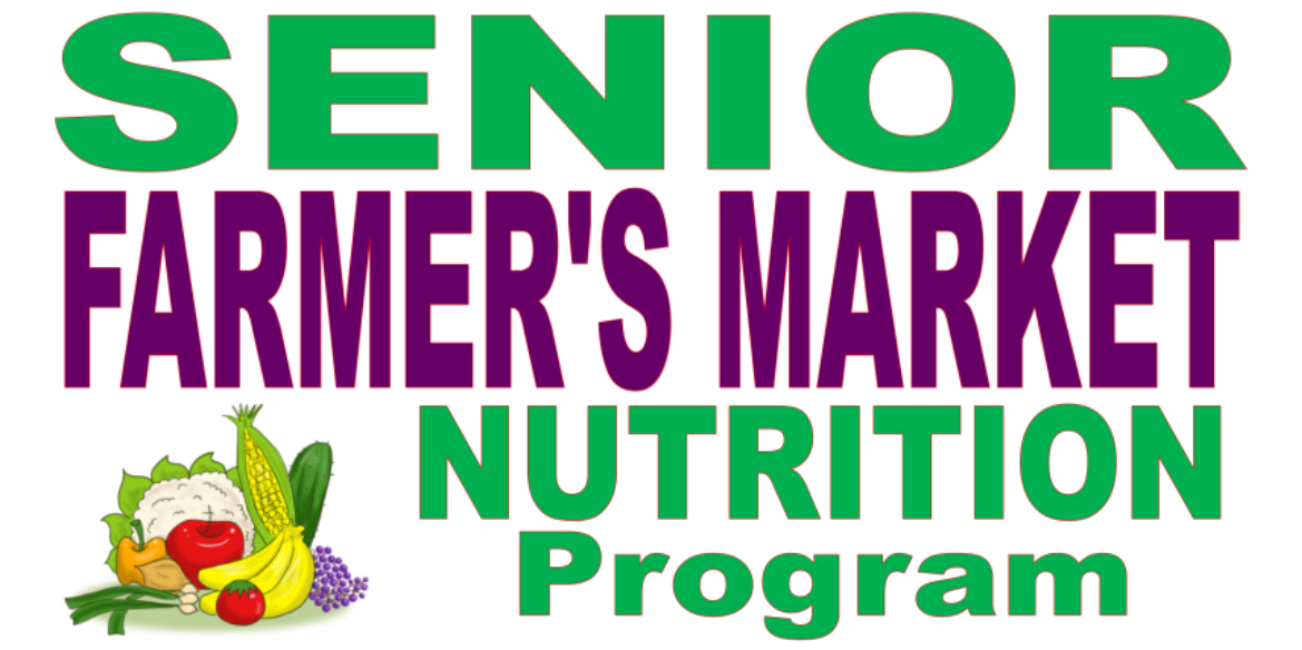 A sign promoting a senior farmer's market nutrition program with large green and purple text, and a small illustration of vegetables including cauliflower, corn, zucchini, banana, grape, and tomato.