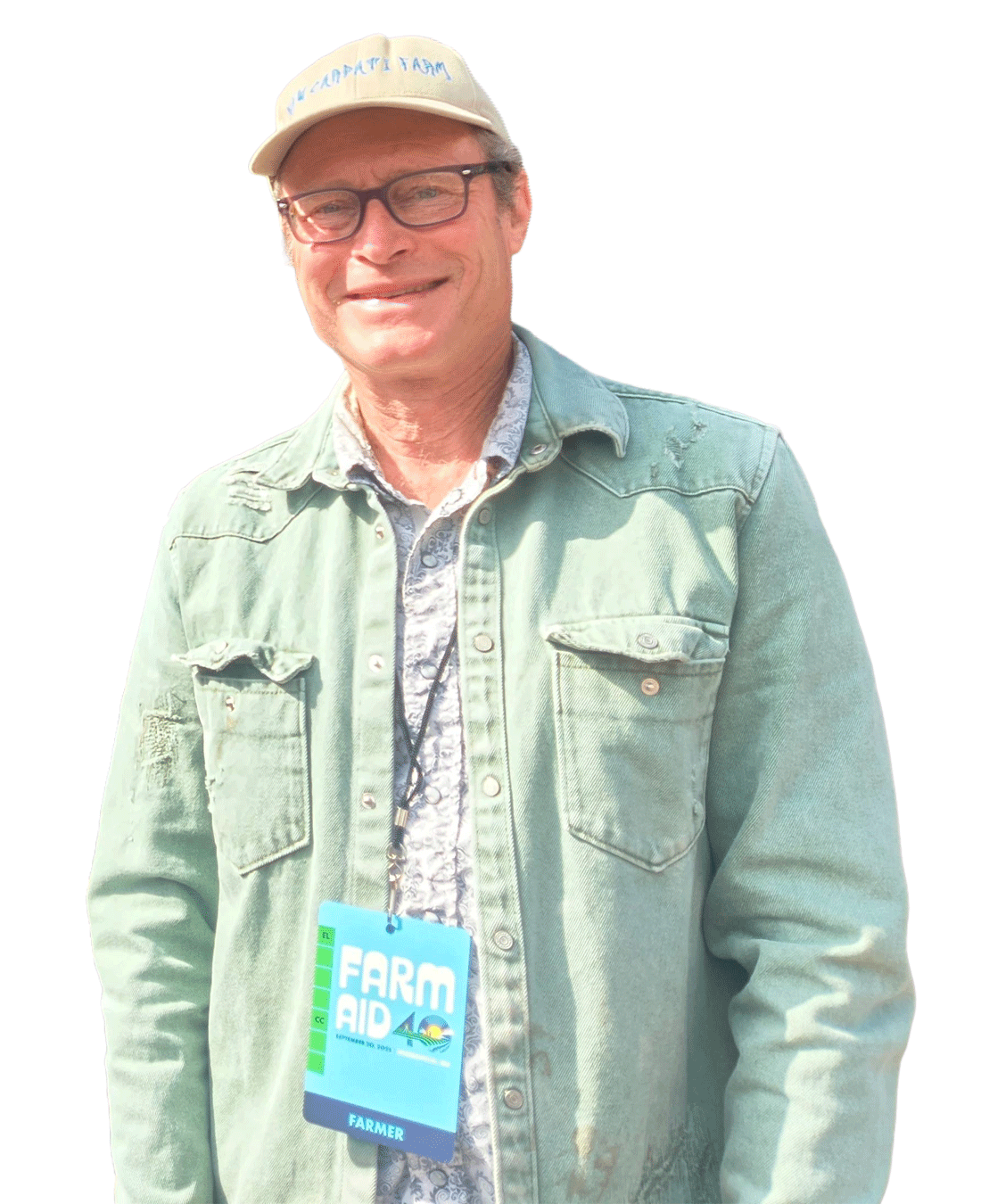 A man wearing glasses, a beige cap, a denim jacket, and a lanyard with a blue badge that says "Farm Aid" and "Farmer".
