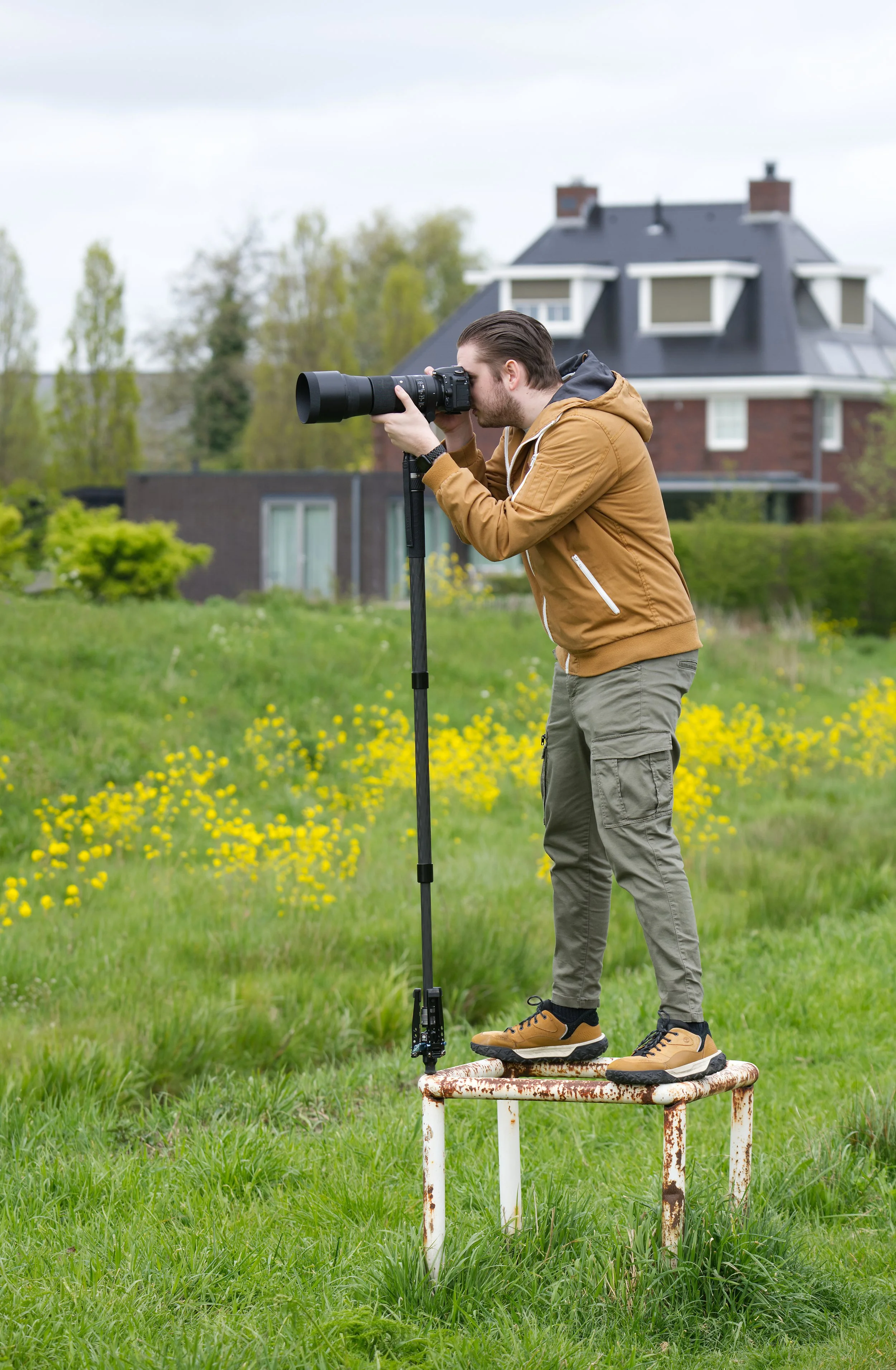 Man staat op een metaalplatform en neemt een foto met een telelens van een ver uitzicht, met een huis en bomen op de achtergrond.