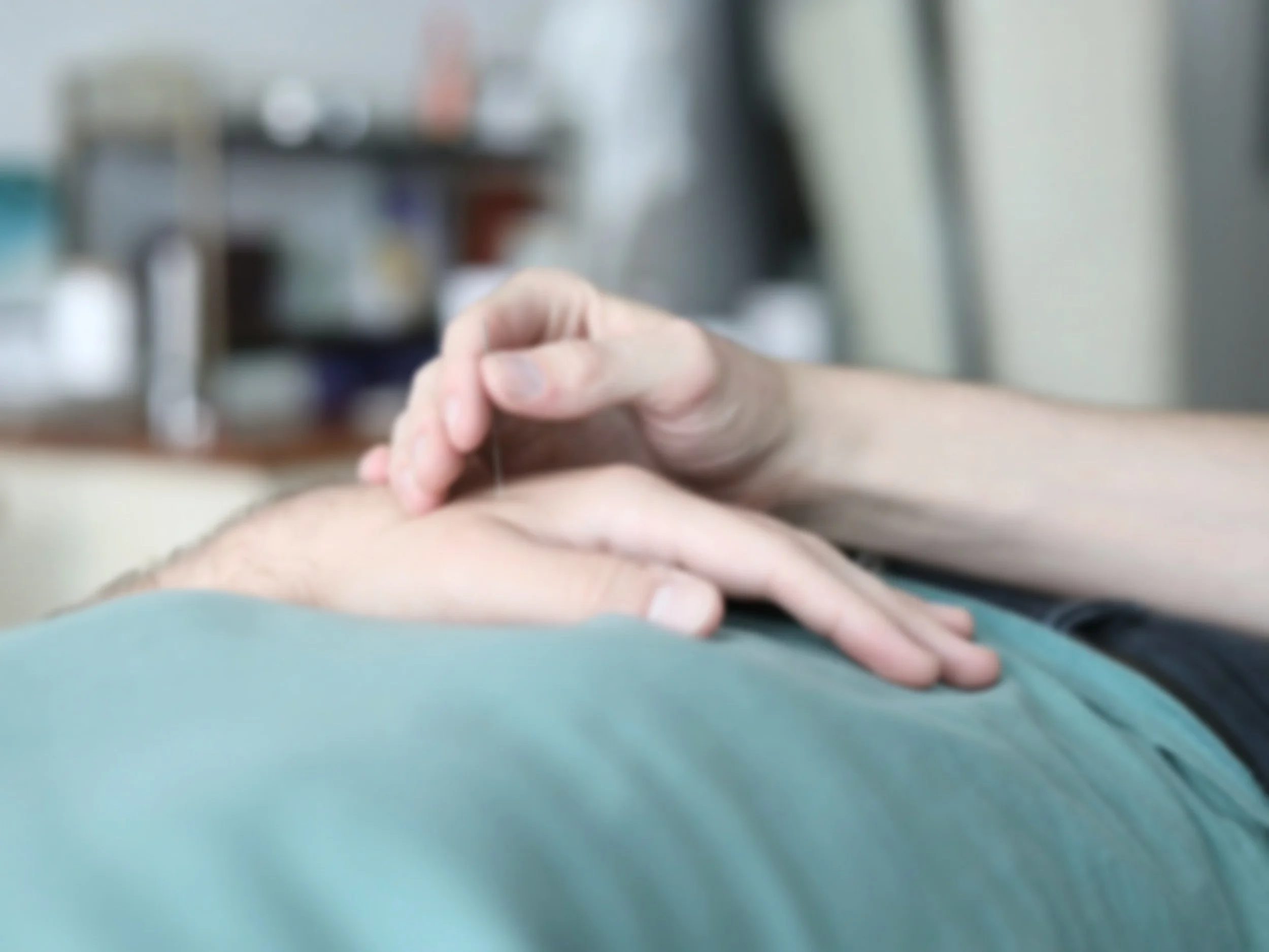 Close-up of a person's hand performing acupuncture on another person's abdominal area in a clinical setting.