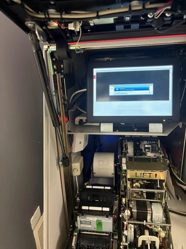 Inside a small electronic or robotic device, showing a computer screen, various wiring, and mechanical components like a lift mechanism and motors.