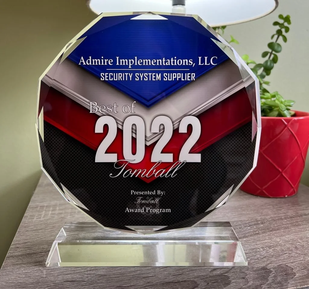 Crystal award plaque for Best of 2022 from Admir Implementations LLC, a security system supplier, placed on a wooden surface with a red plant pot and green plant in the background.