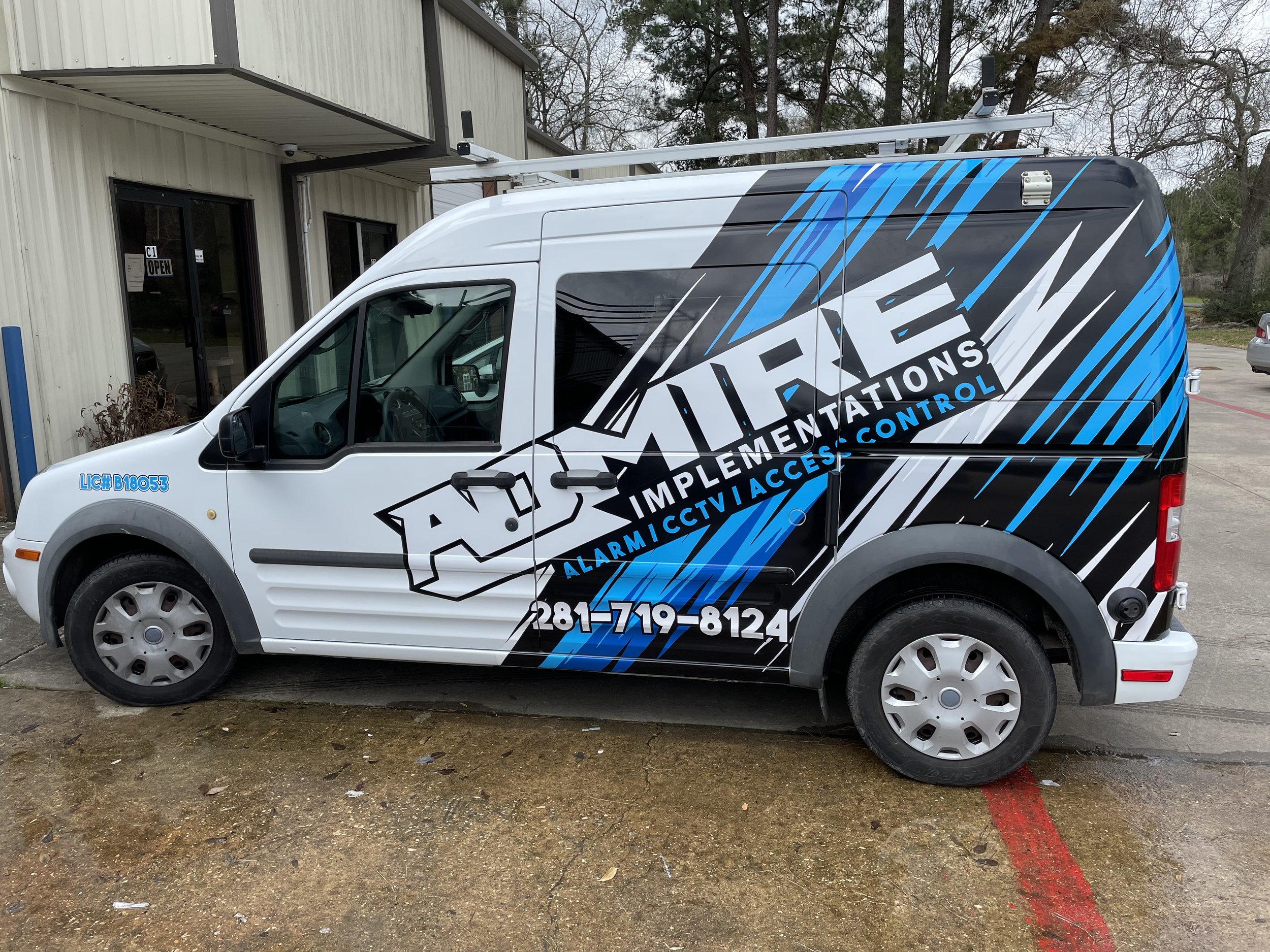 Company van for Advanced Implementations with signage indicating services such as alarm, CCTV, access control, and more, parked outside a commercial building.
