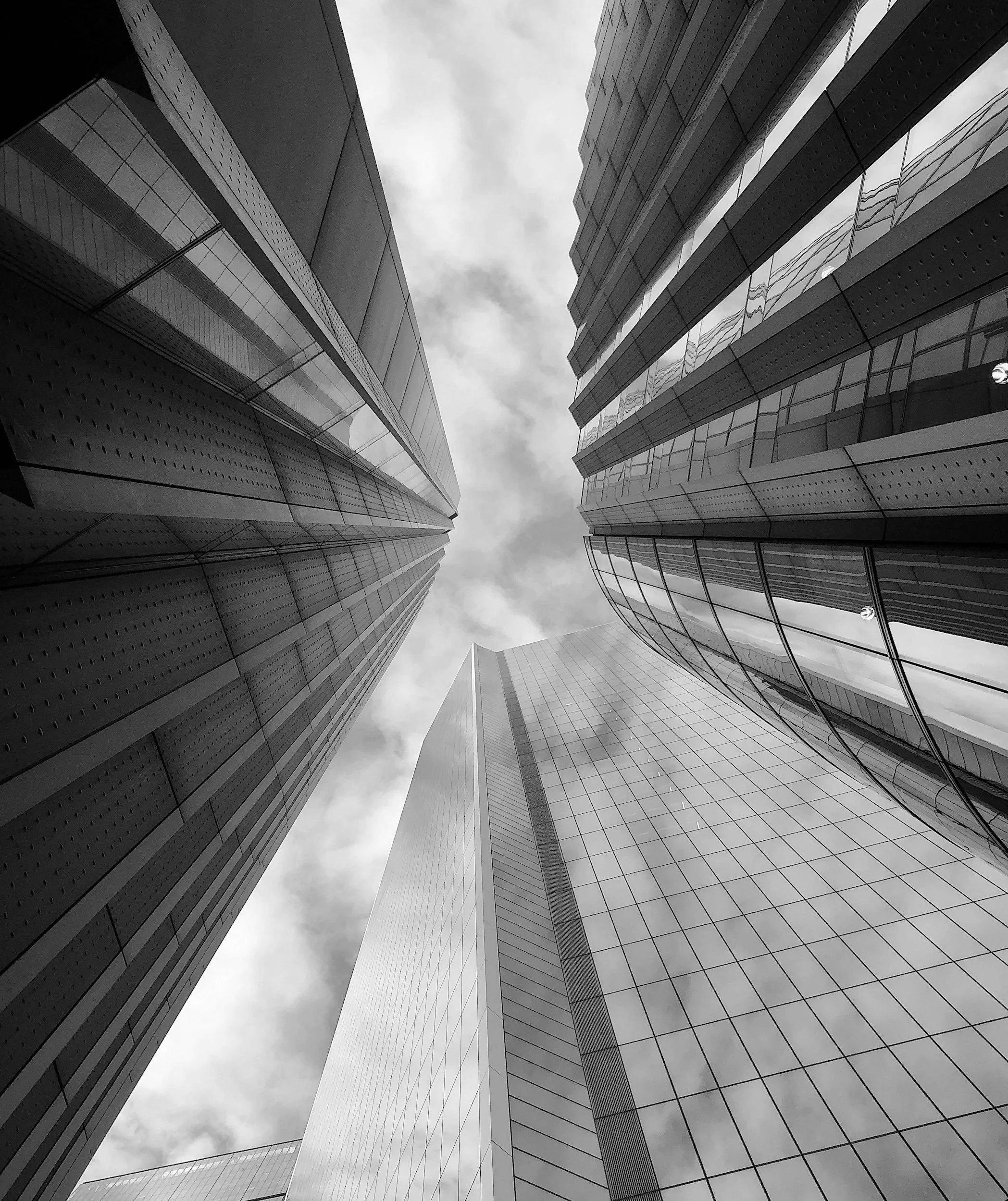 Low-angle black and white photo of modern skyscrapers with reflective glass windows reflecting sky and clouds.