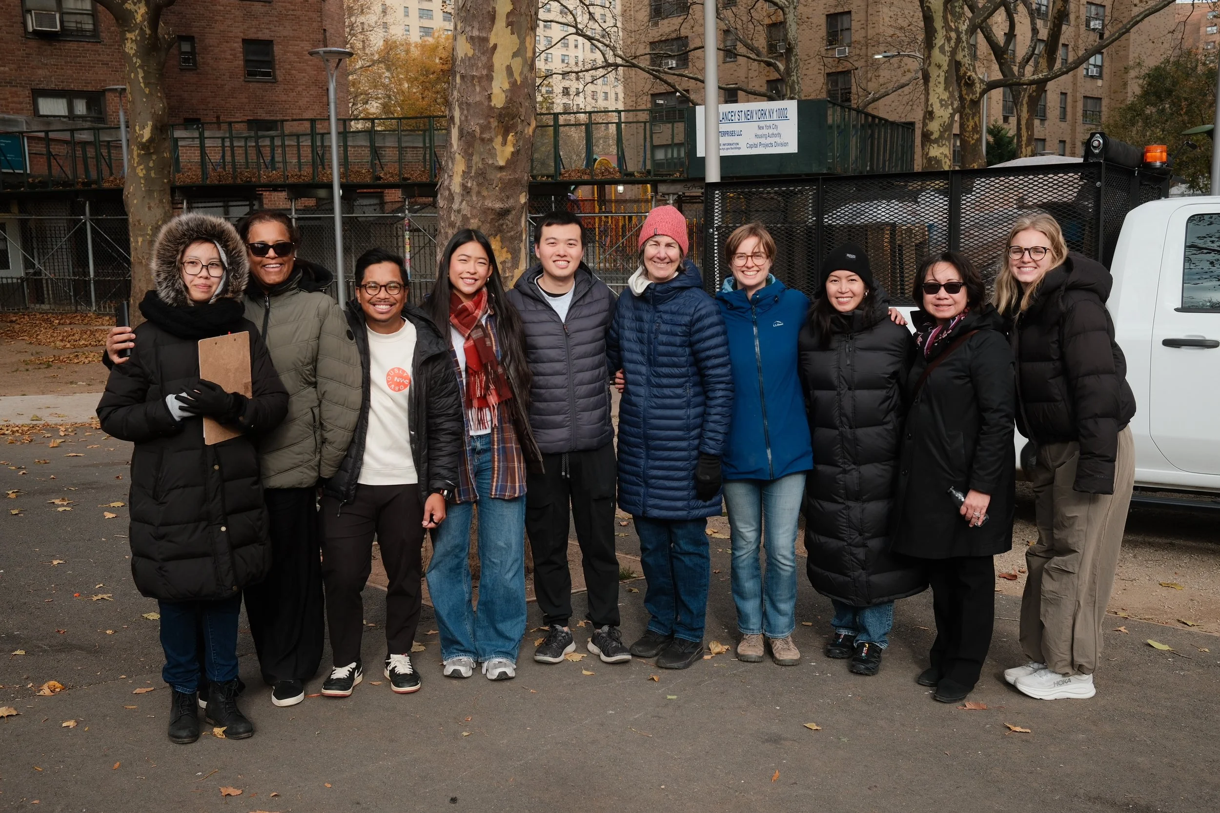Group of eleven people standing together outdoors in fall, dressed warmly, smiling for the camera.