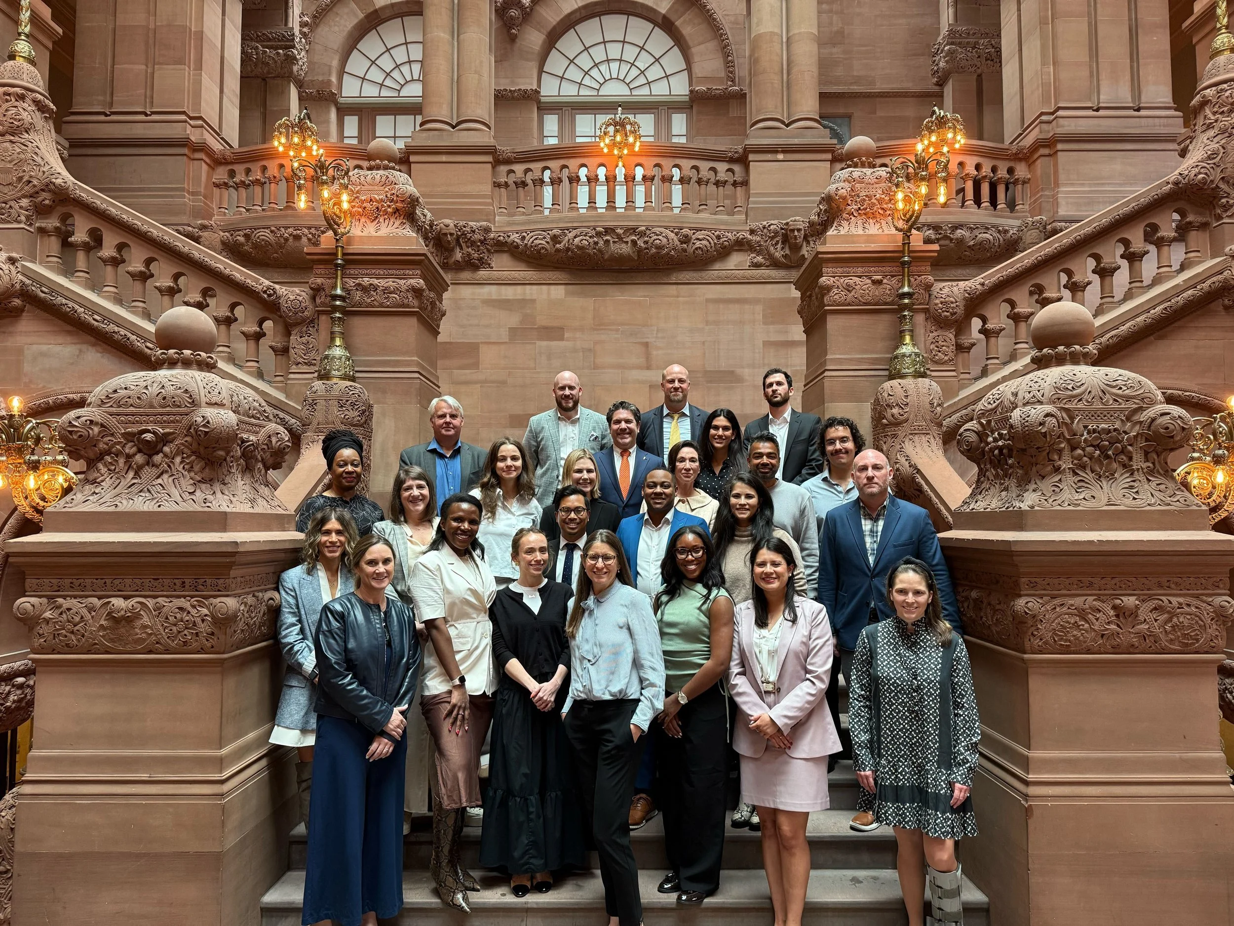 Group of diverse professionals standing on decorative staircase inside a historic building with ornate architecture and warm lighting.