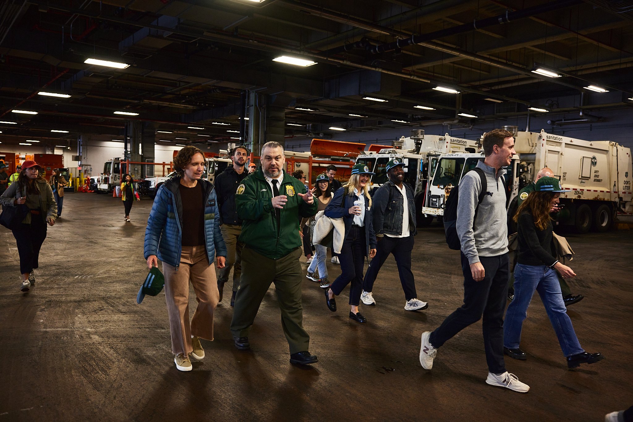 Group of people touring an indoor industrial facility with utility vehicles in the background.