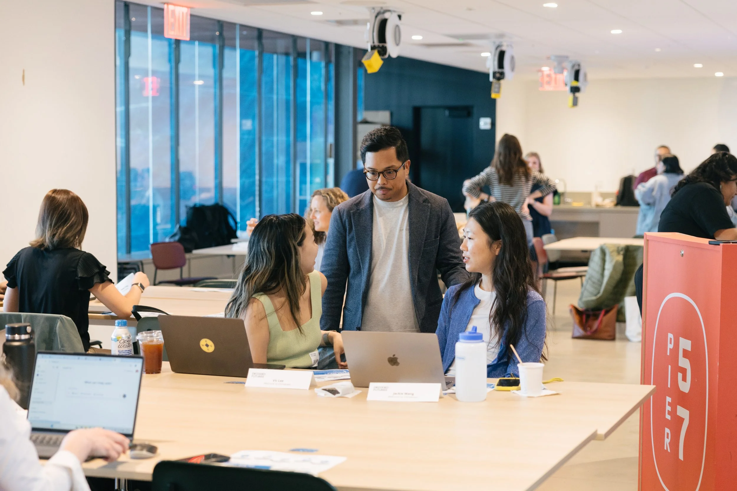 People working and conversing in a modern conference room or coworking space, with laptops and beverages on the tables.