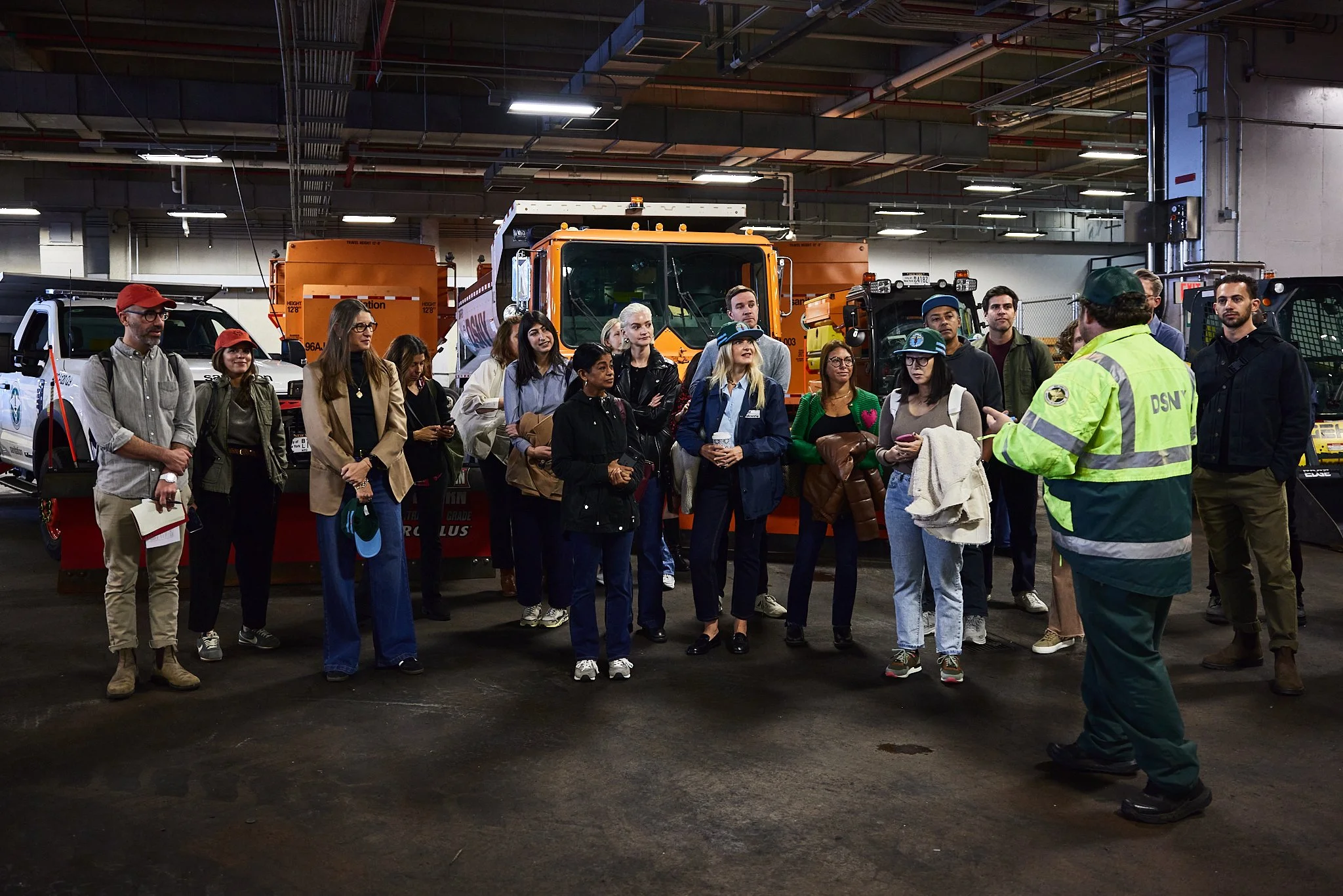 Group of people listening to a guide inside a garage with large utility vehicles and equipment.