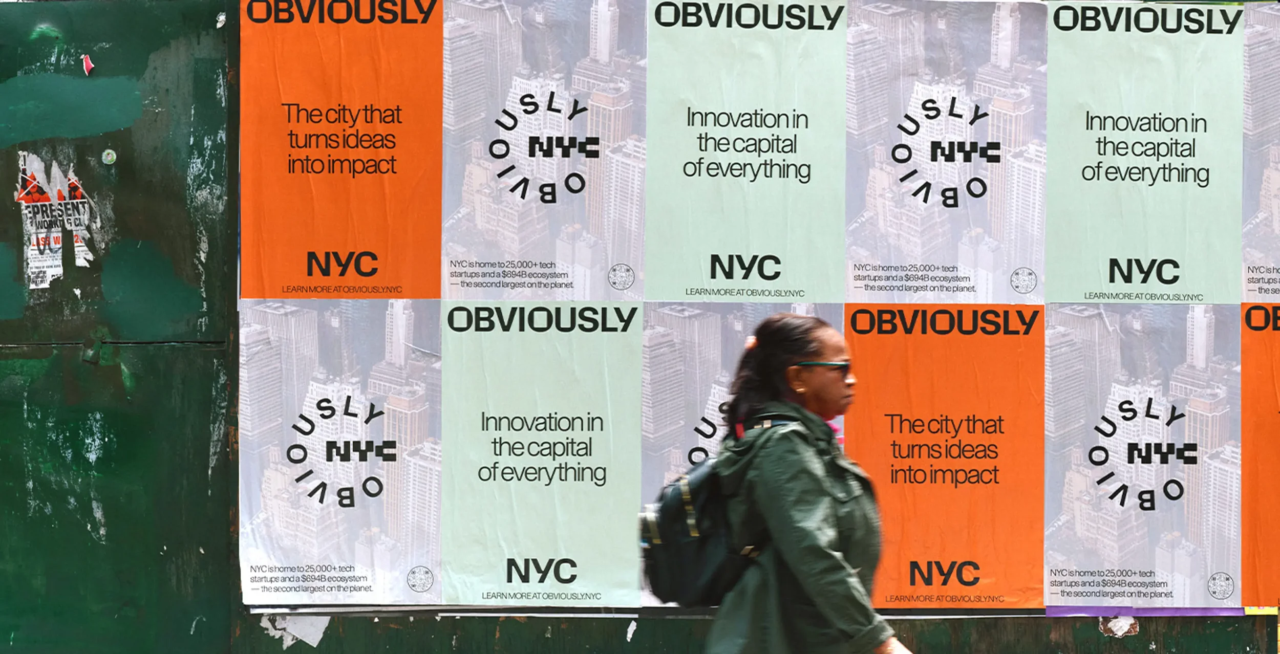 A woman walking past a colorful advertisement poster on a city street wall. The posters promote NYC with phrases like 'The city that turns ideas into impact' and 'Innovation in the capital of everything,' featuring the NYC logo and information about 