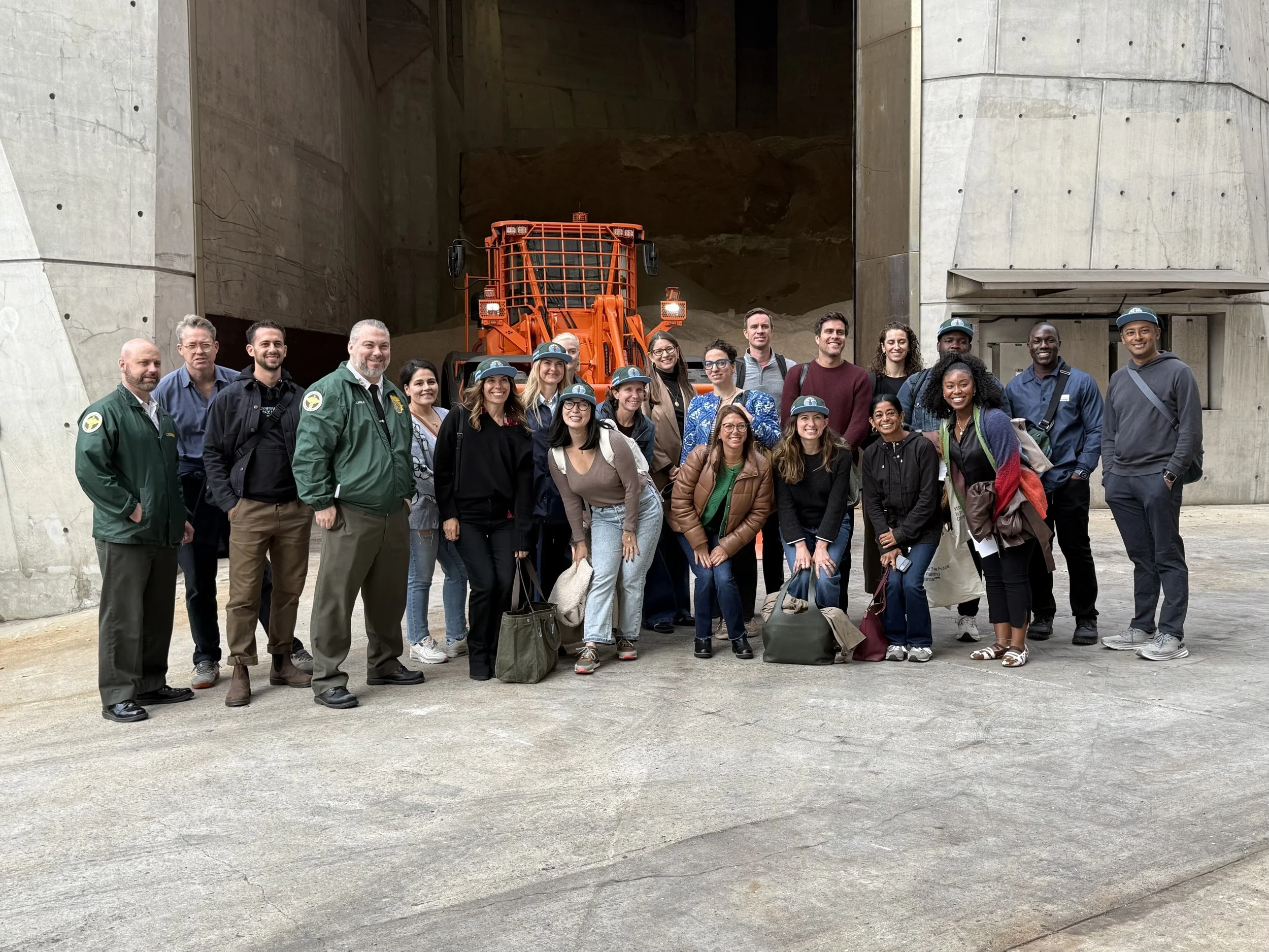 Group of people posing for a photo in front of an orange construction vehicle inside a concrete structure.