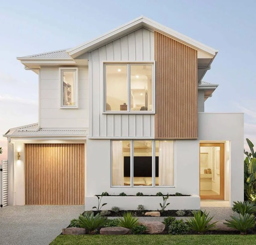 Modern two-story house with white exterior walls, large front windows, and wooden accents on the facade. There's a garage with a wooden door on the left and a small garden with plants in front.