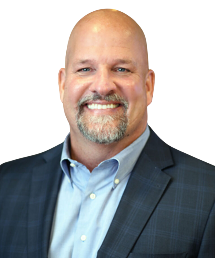 A man with a bald head and a gray beard smiling, wearing a dark checkered suit jacket and a light blue dress shirt against a white background.