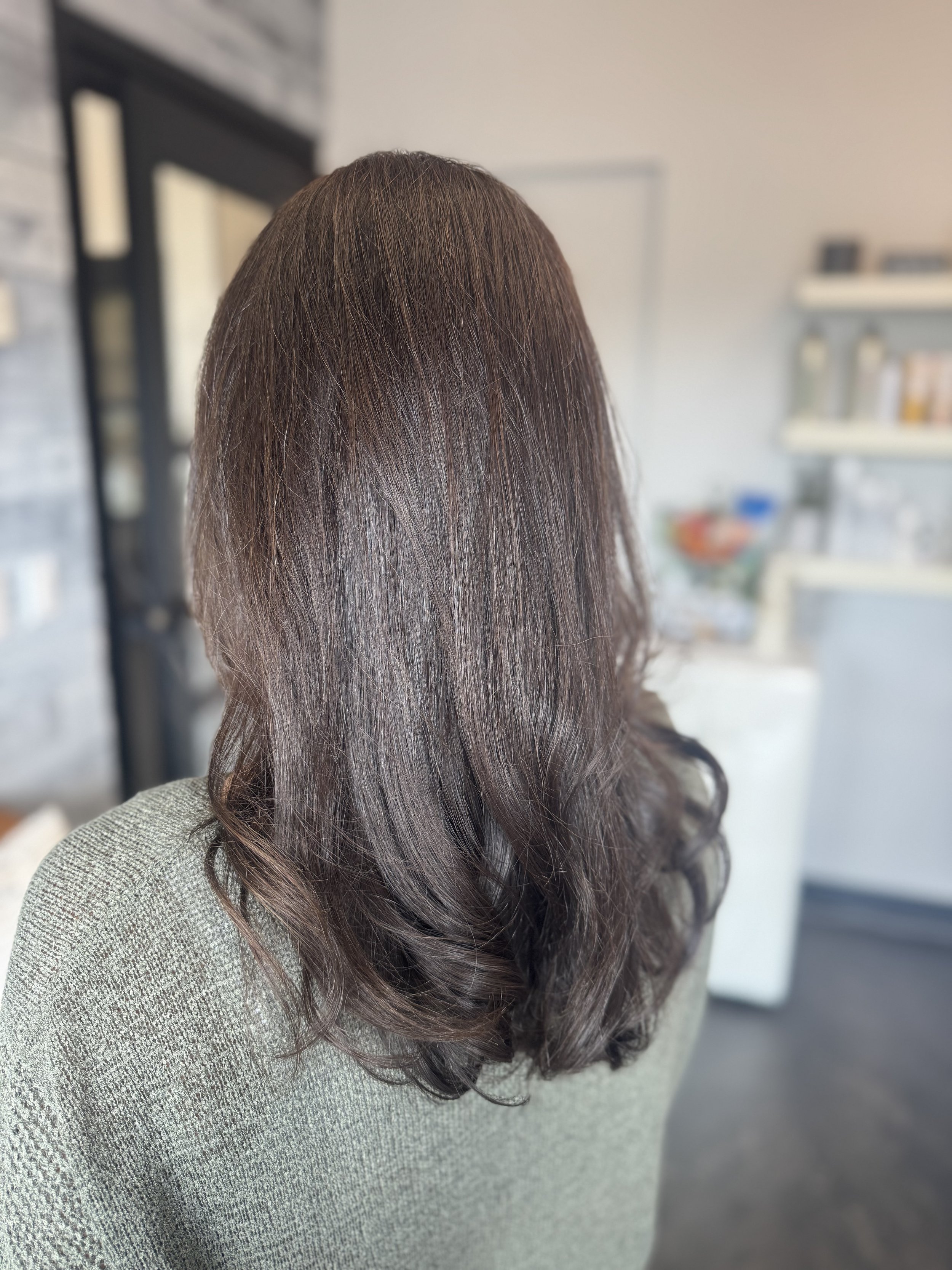 Back view of a woman with medium-length, wavy brown hair in a cozy indoor setting.